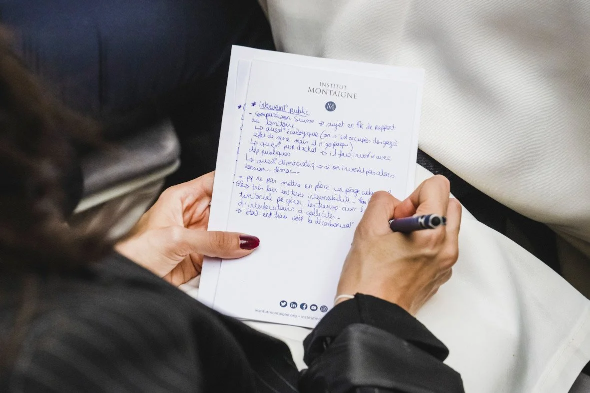 Une personne écrit sur une feuille de papier. La feuille est en-tête de l'Institut Montagne et comporte des notes manuscrites en français.