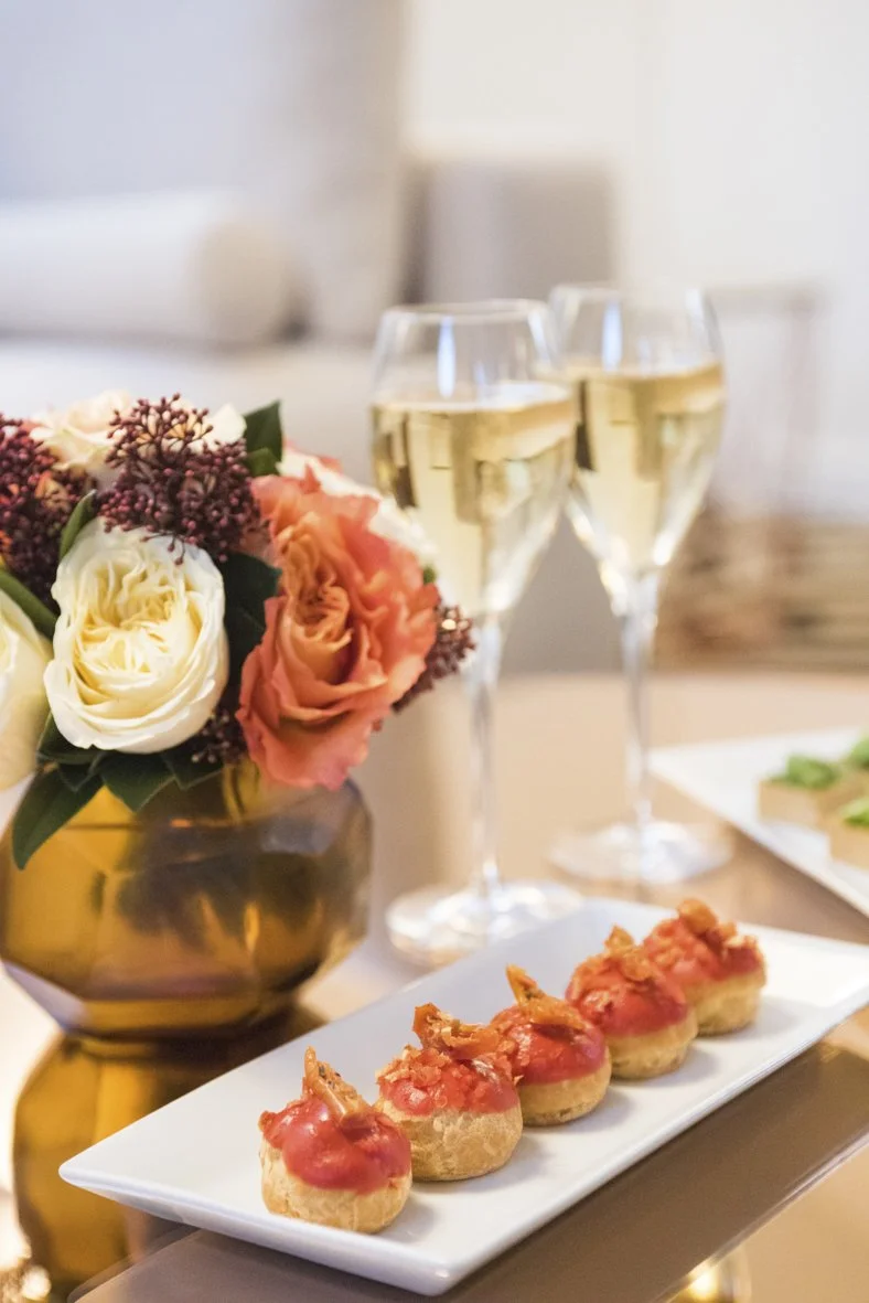 Vase avec fleurs, deux verres de champagne, et des petites tartes sur une assiette