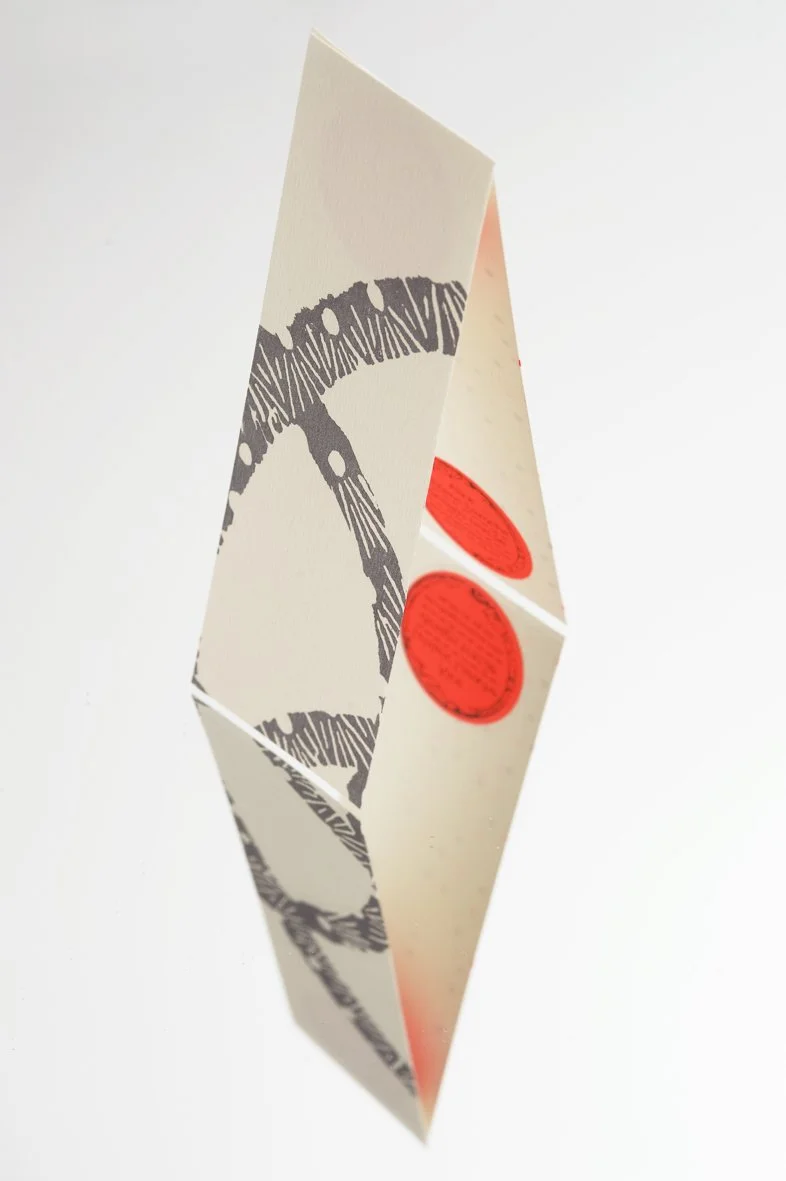 Une carte pliée en forme de diamant avec une illustration noire d'une chaîne ou câble et deux cercles rouges sur une face.