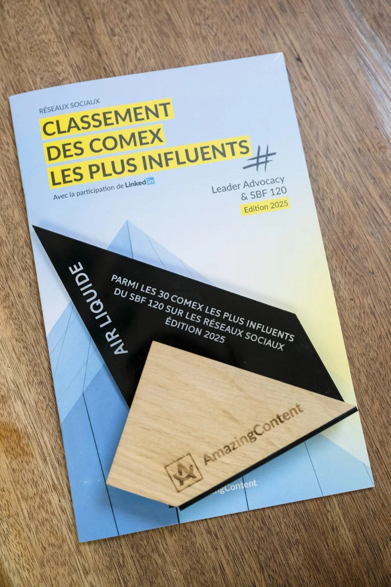 Brochure bleu et blanc sur le classement des influenceurs COMEX avec participation LinkedIn, édition 2025, posé sur un bureau en bois, avec un bloc-notes en bois portant le logo Amazingcontent.