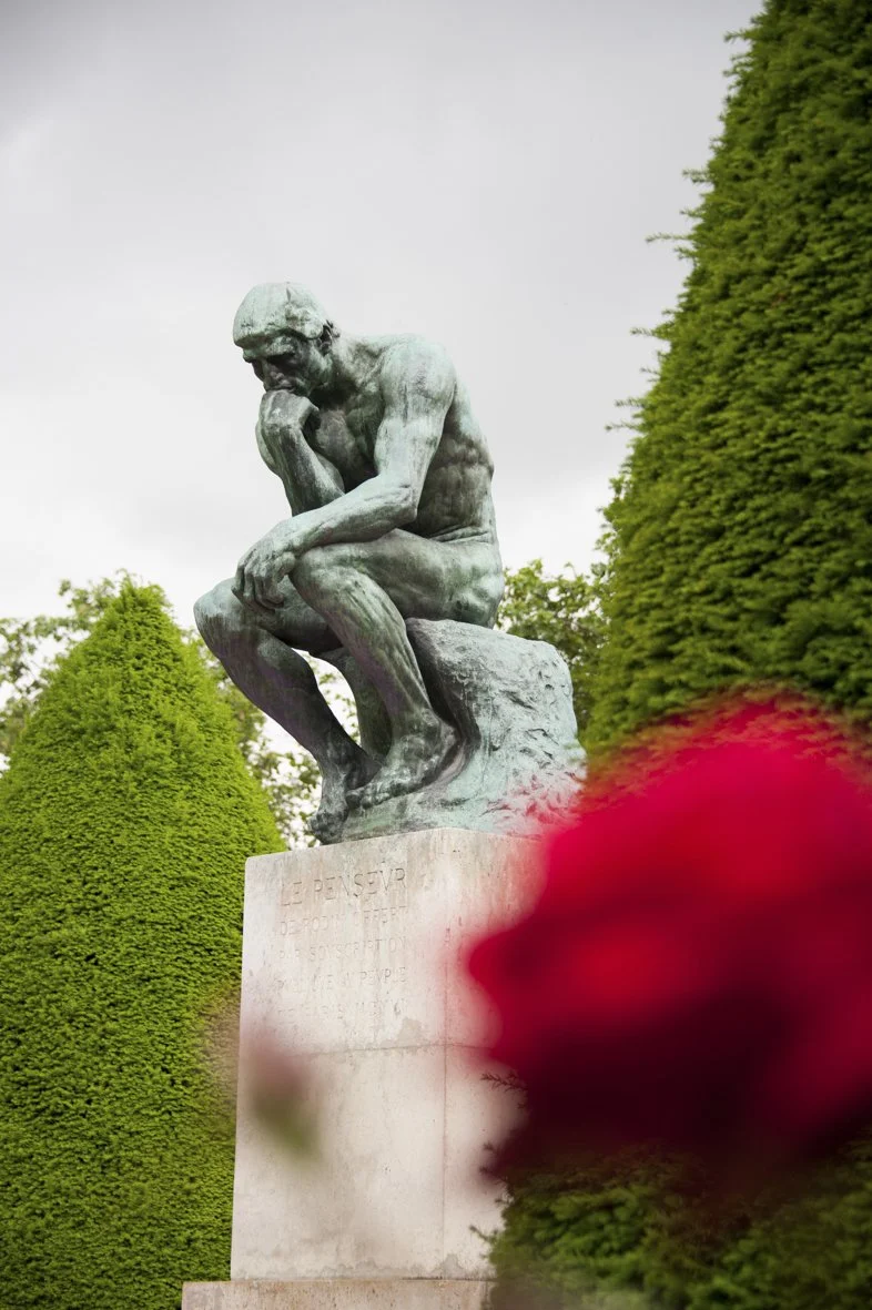 Statue de Discobole de face, dans un jardin avec des buissons verts et un ciel nuageux