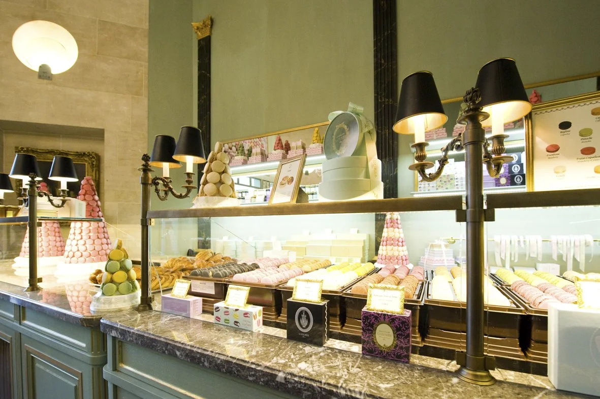 Vitrine d'pâtisserie avec des macarons multicolores, éclairés par des lampes noires, dans une boutique élégante au décor vintage.