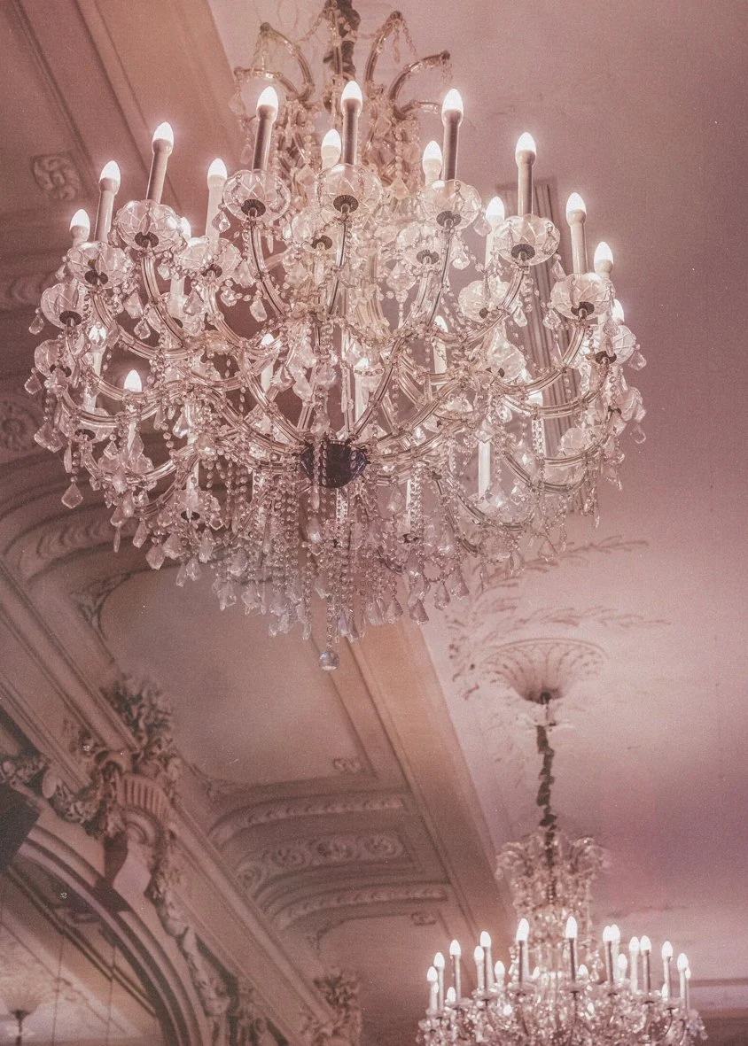 Deux grands lustres en cristal suspendus au plafond orné de moulures décoratives.