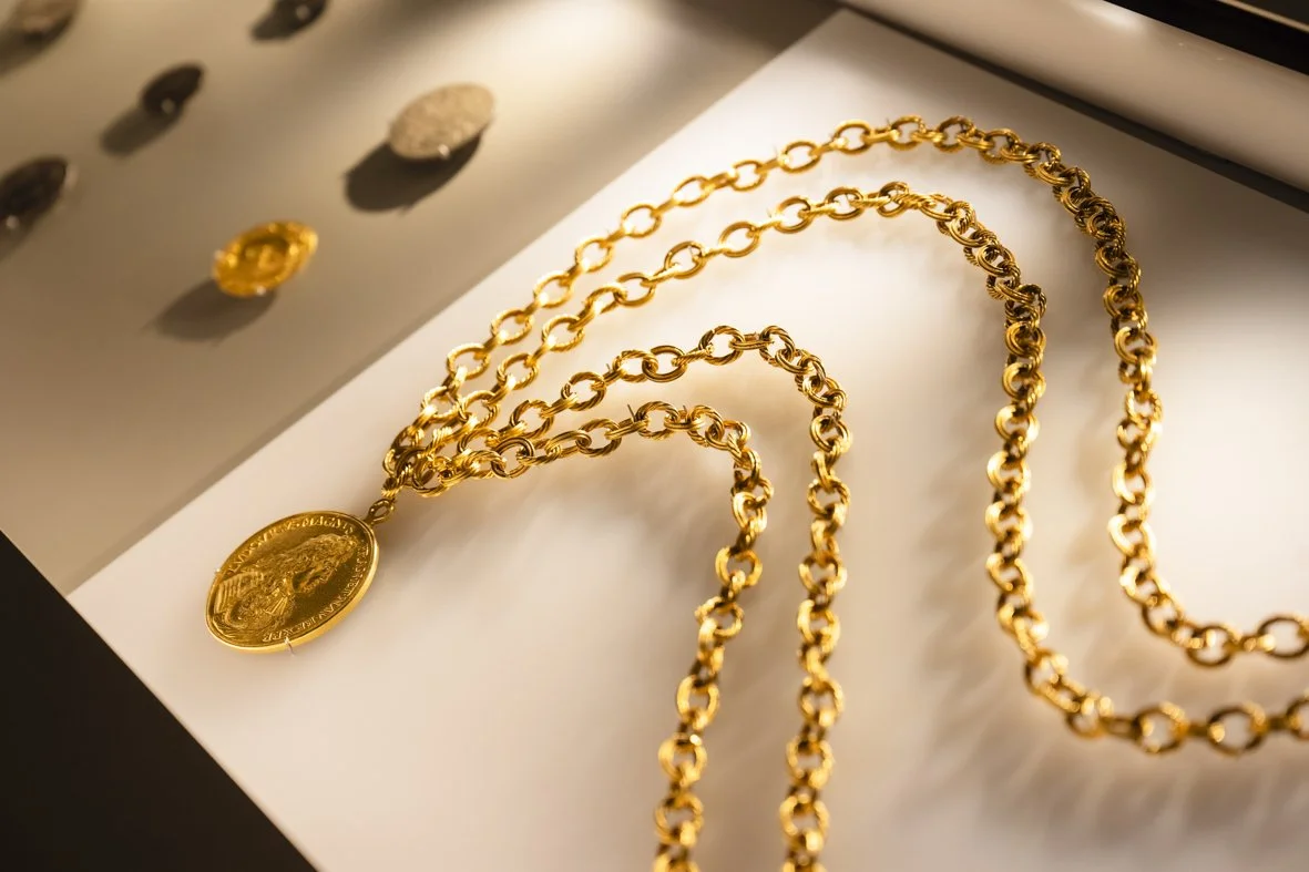 Collier en or avec une médaille ancienne, posé sur une surface blanche, avec d'autres bijoux en arrière-plan.