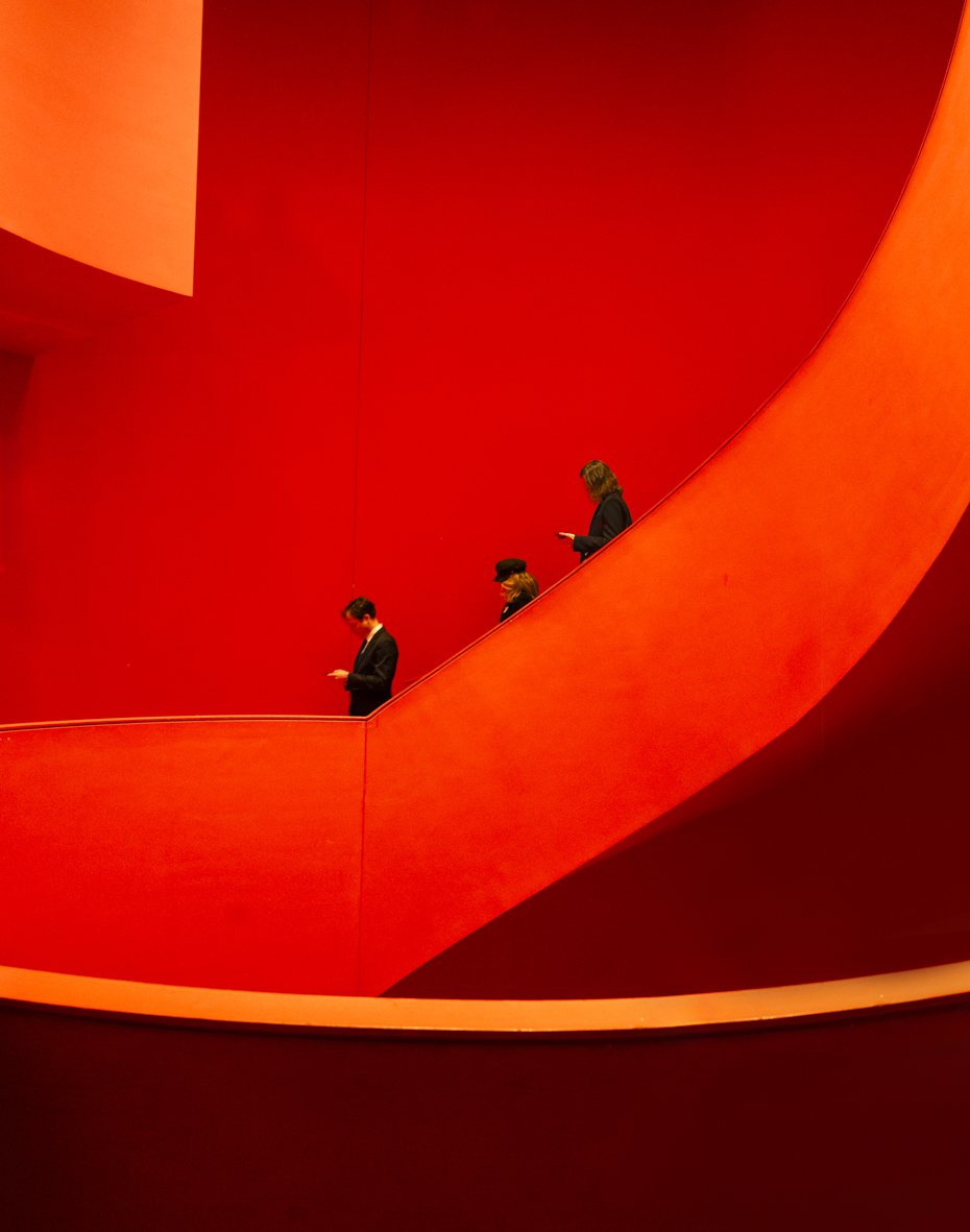 Trois personnes debout sur une rampe rouge courbée dans un bâtiment moderne.