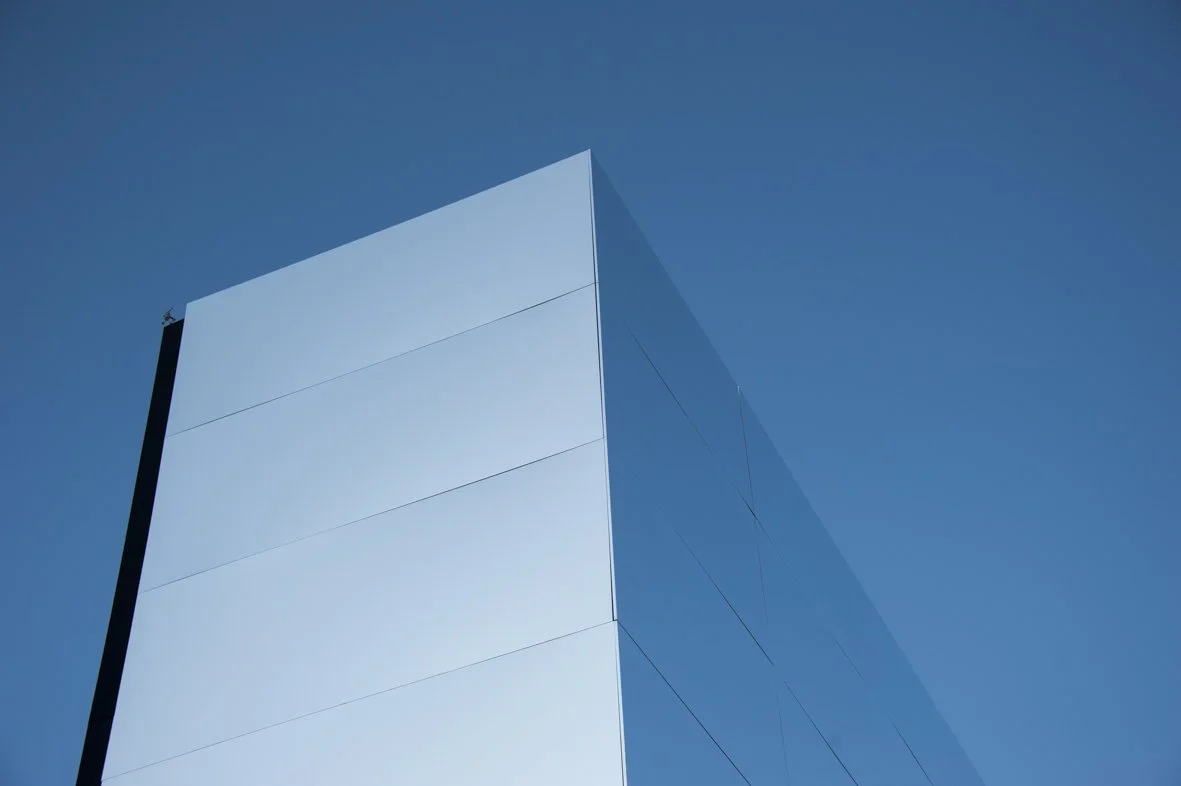 Une photo d'un bâtiment moderne avec une façade en verre brillant, sous un ciel bleu clair.