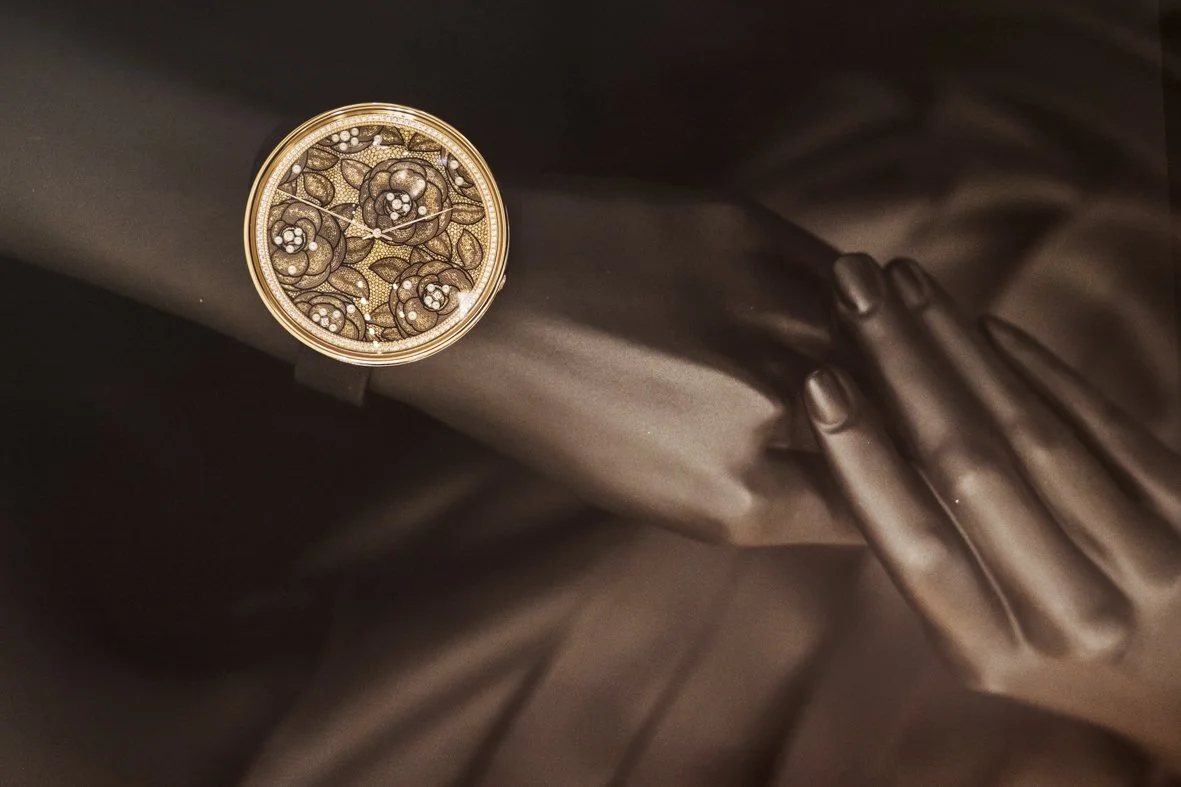 Une montre en or posée sur un tissu en satin, avec une main délicate à côté.