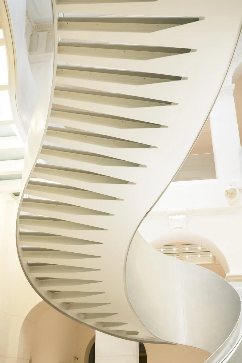 Escalier hélicoïdal blanc vu de dessous, situé dans un intérieur élégant avec des arches et des détails classiques.