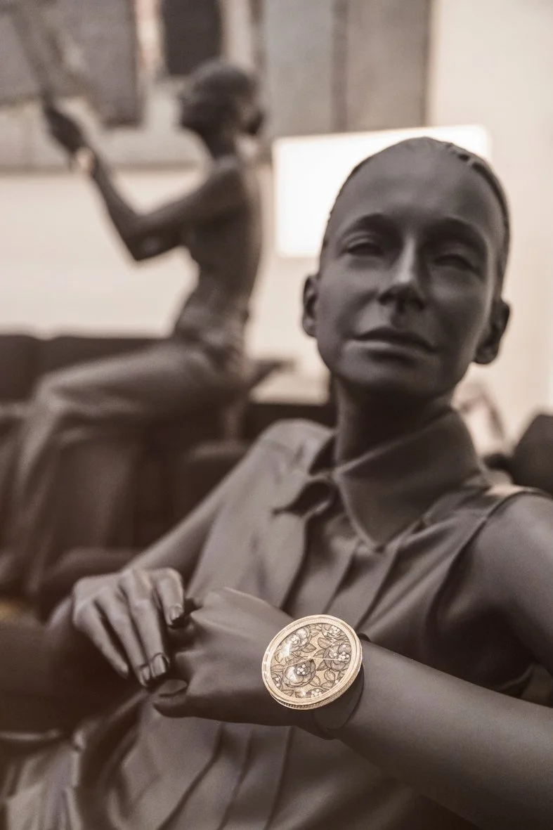 Statue en bronze représentant deux figures humaines, une en premier plan portant un bracelet or, et une autre en arrière-plan assise et levant un bras.