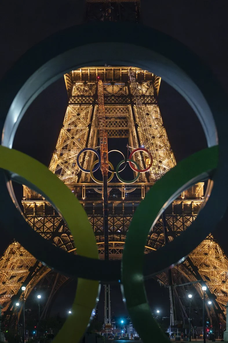 La Tour Eiffel illuminée lors des Jeux Olympiques, vue de bas avec les anneaux olympiques en premier plan.