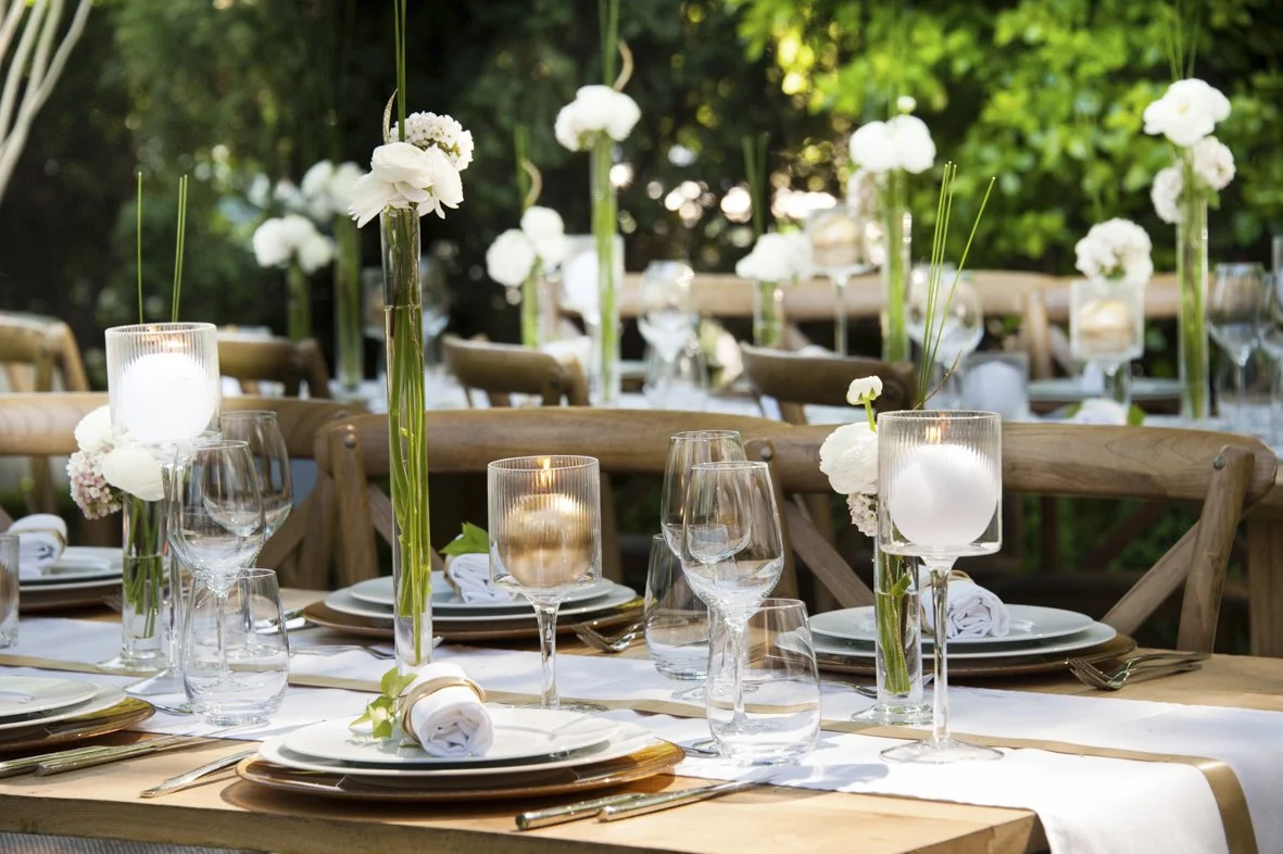Table décorée pour un événement en plein air avec fleurs blanches, bougies et vaisselle élégante.