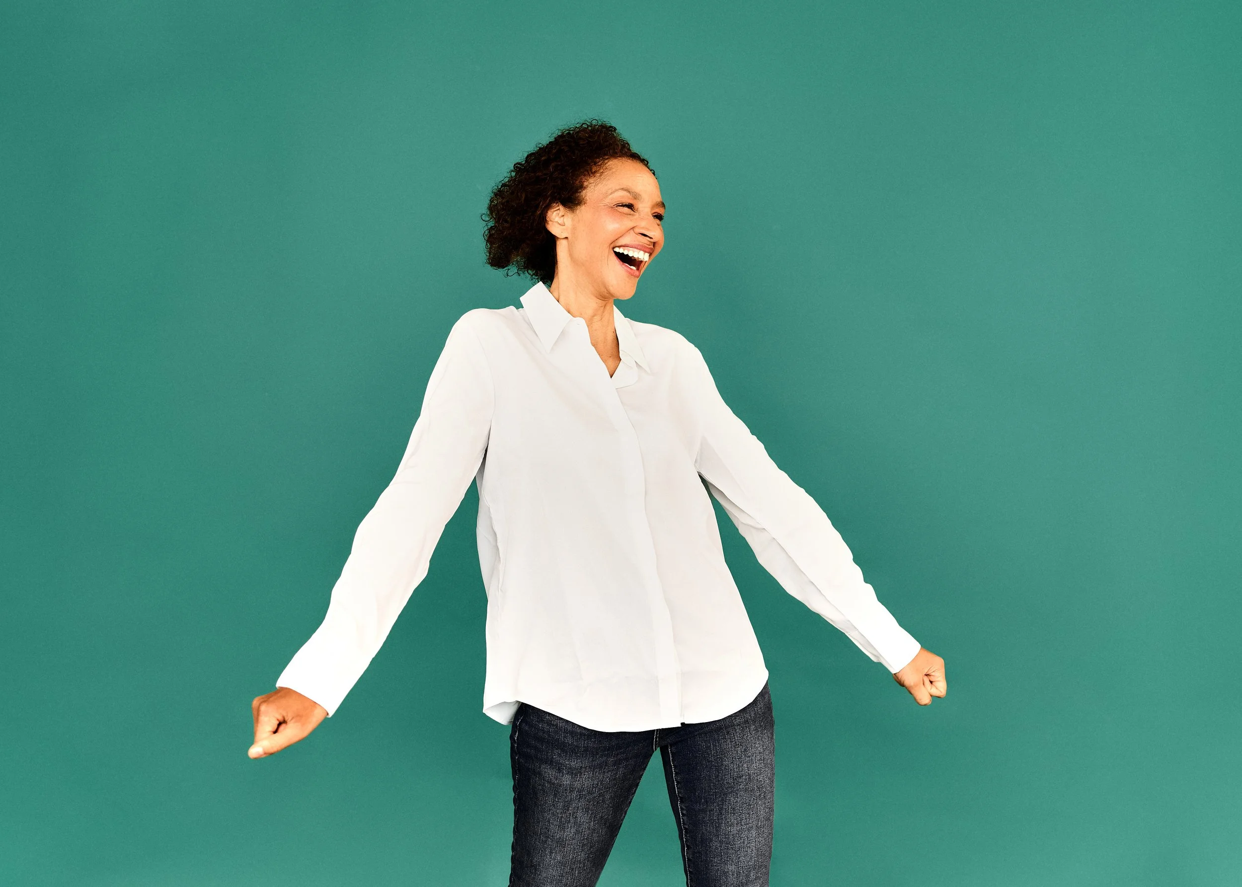 Gaëlle Georges lacht und trägt eine weiße Bluse und dunkle Jeans vor einem grünen Hintergrund.