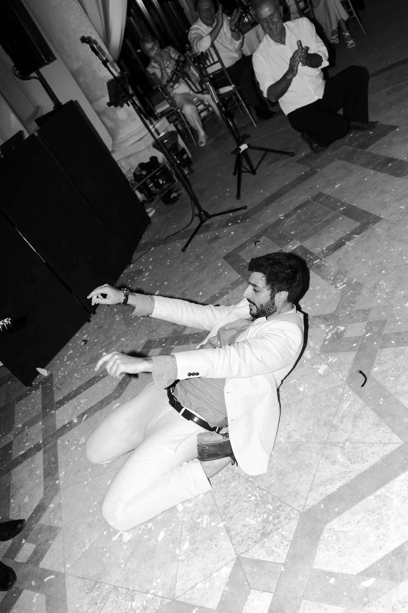 Man dancing on the floor at a party or celebration, with musical instruments and other guests in the background.
