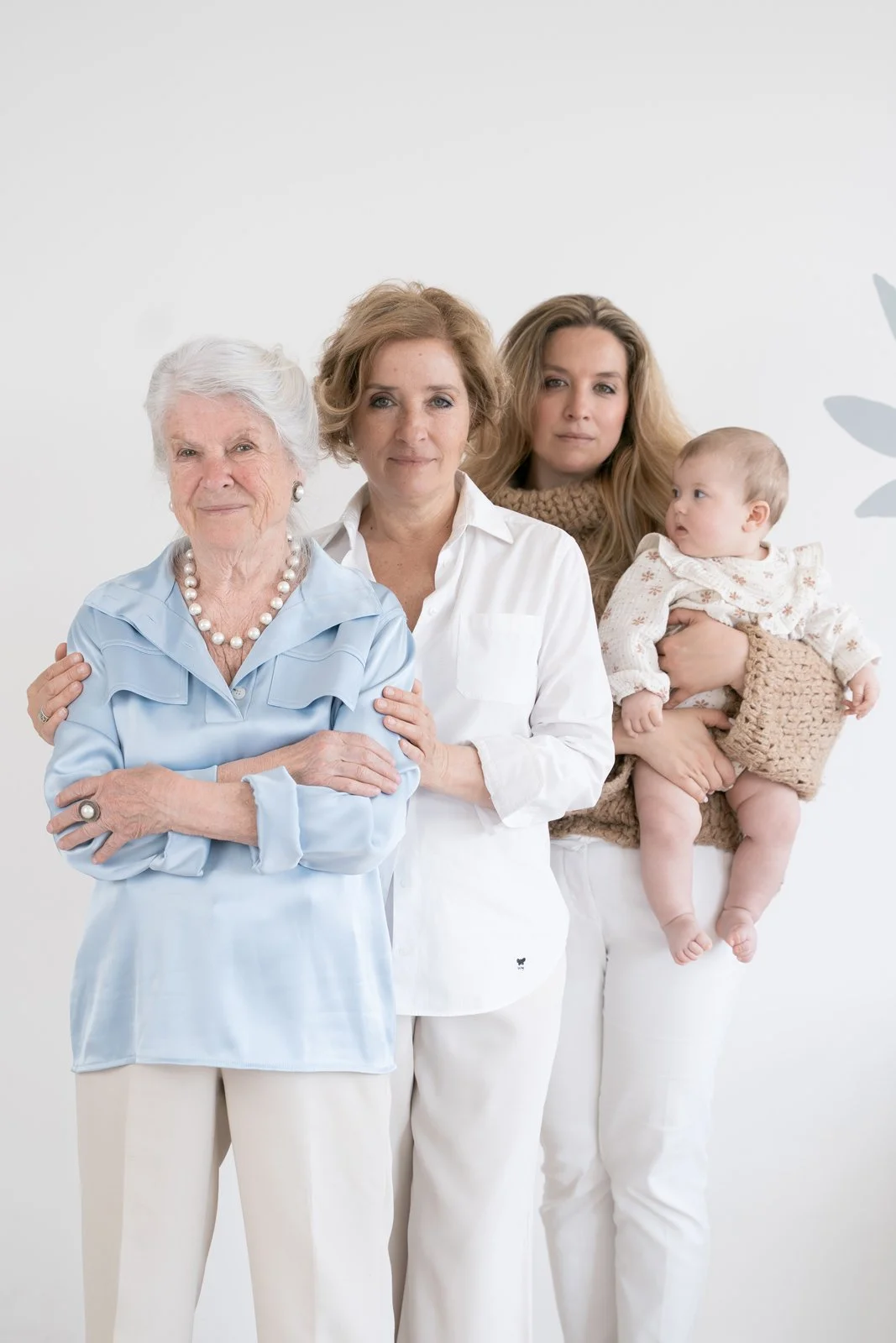 Four generations of women, including an elderly woman, middle-aged women, and a baby, standing together against a plain white background.