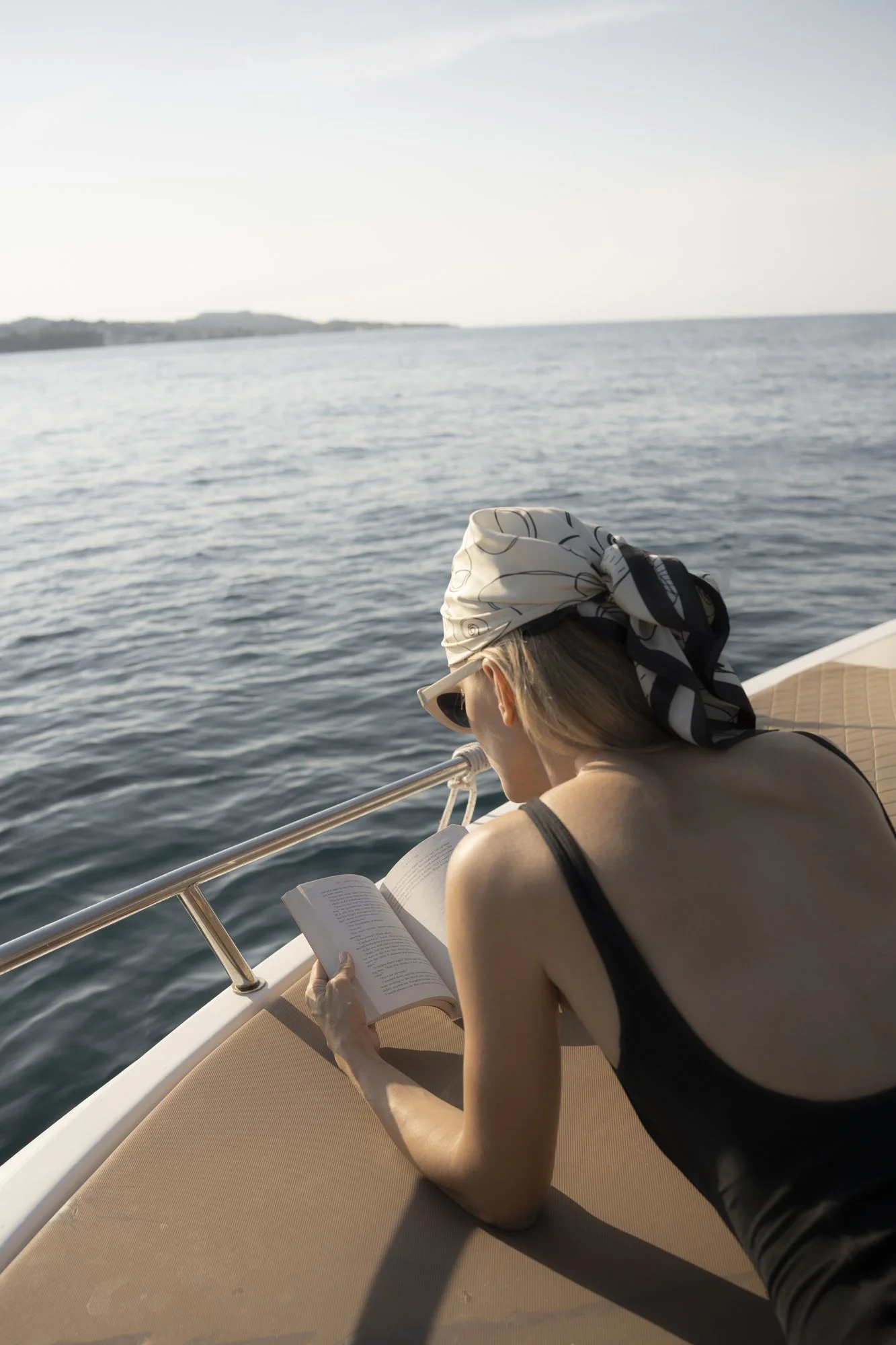 A woman relaxing on a boat, reading a book, with the ocean in the background.