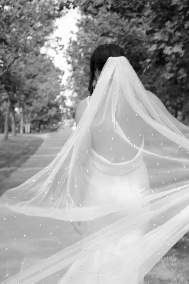 A woman wearing a bridal gown with a long train outdoors on a pathway lined with trees.