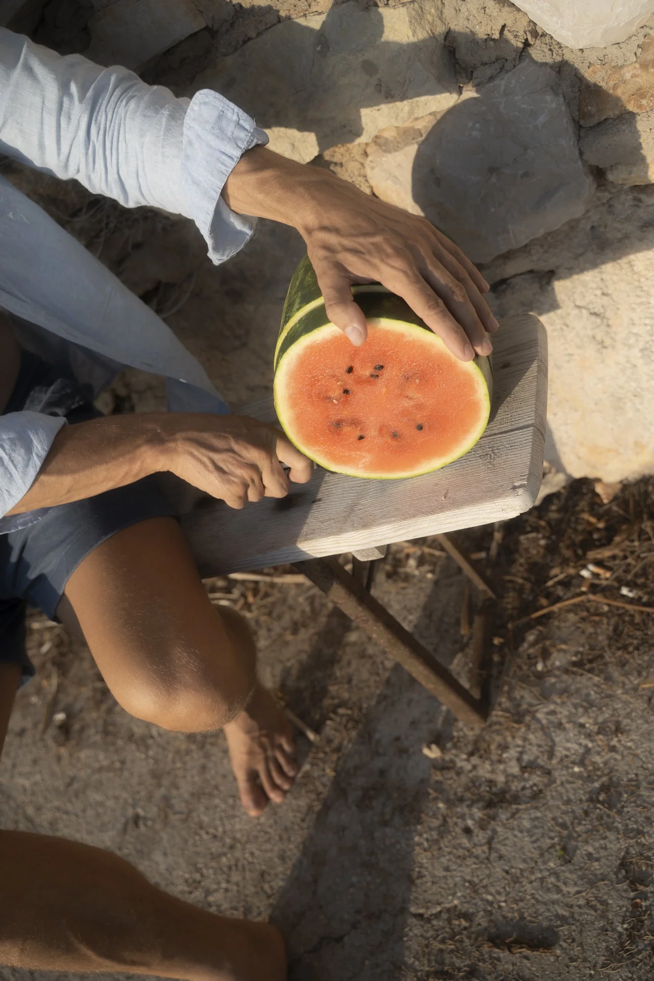 Person cutting a watermelon on a wooden board outdoors.