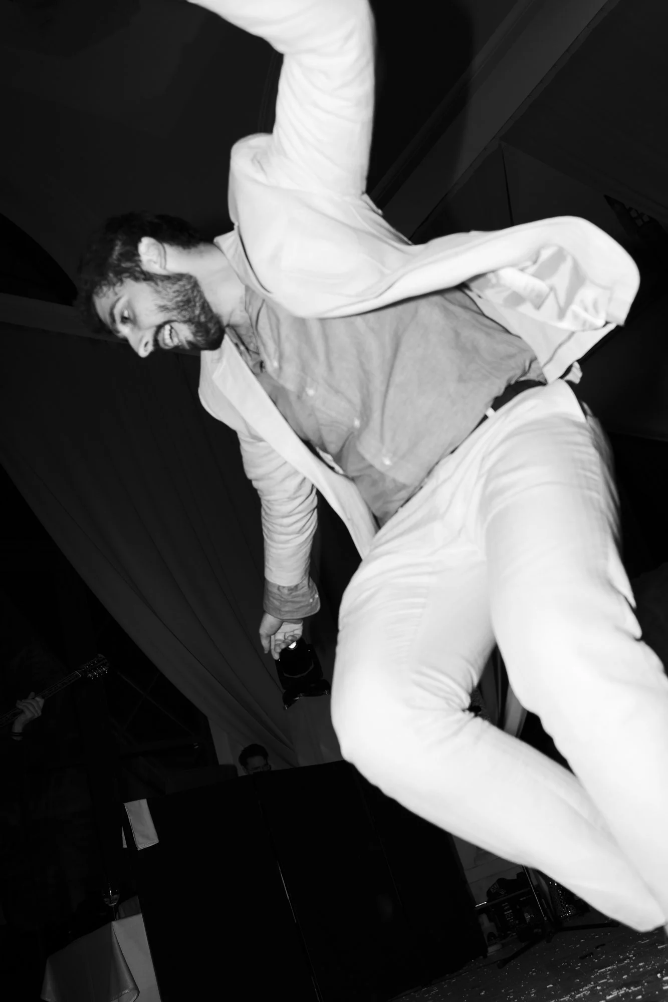 A man with a beard and white jacket smiling while dancing at a party.