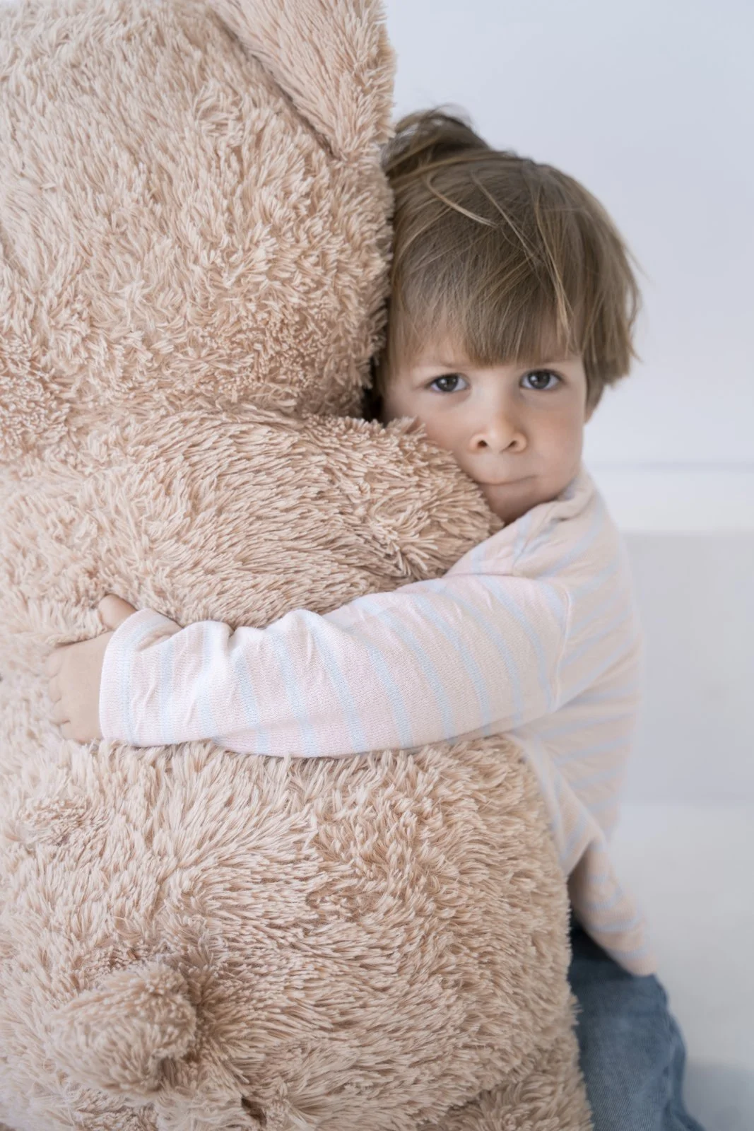 Young boy hugging a large plush teddy bear, looking at the camera with a neutral expression.