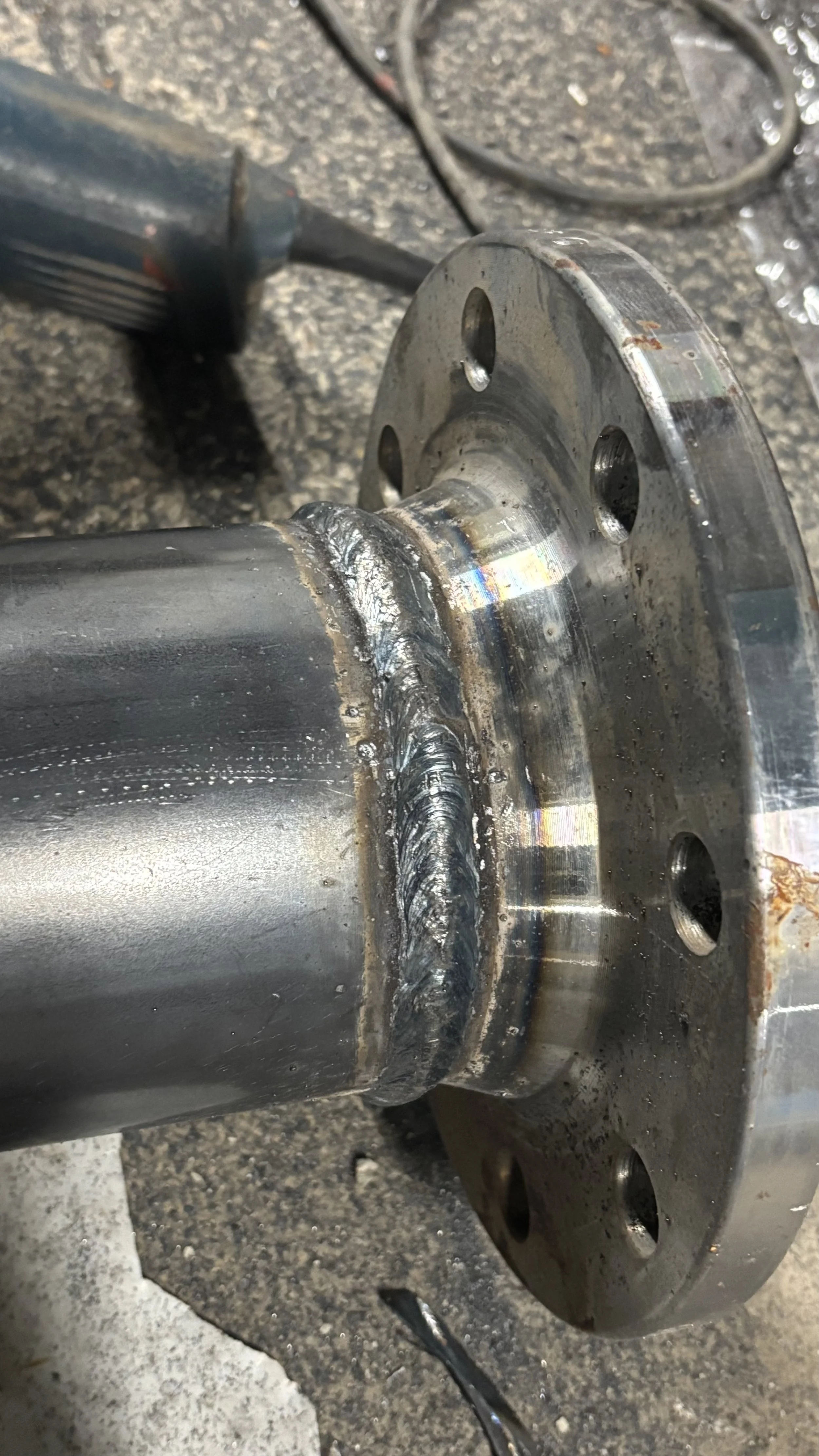 Vue rapprochée d'un axe de machine avec une soudure neuve et une surface métallique polie, posée sur un sol en béton.