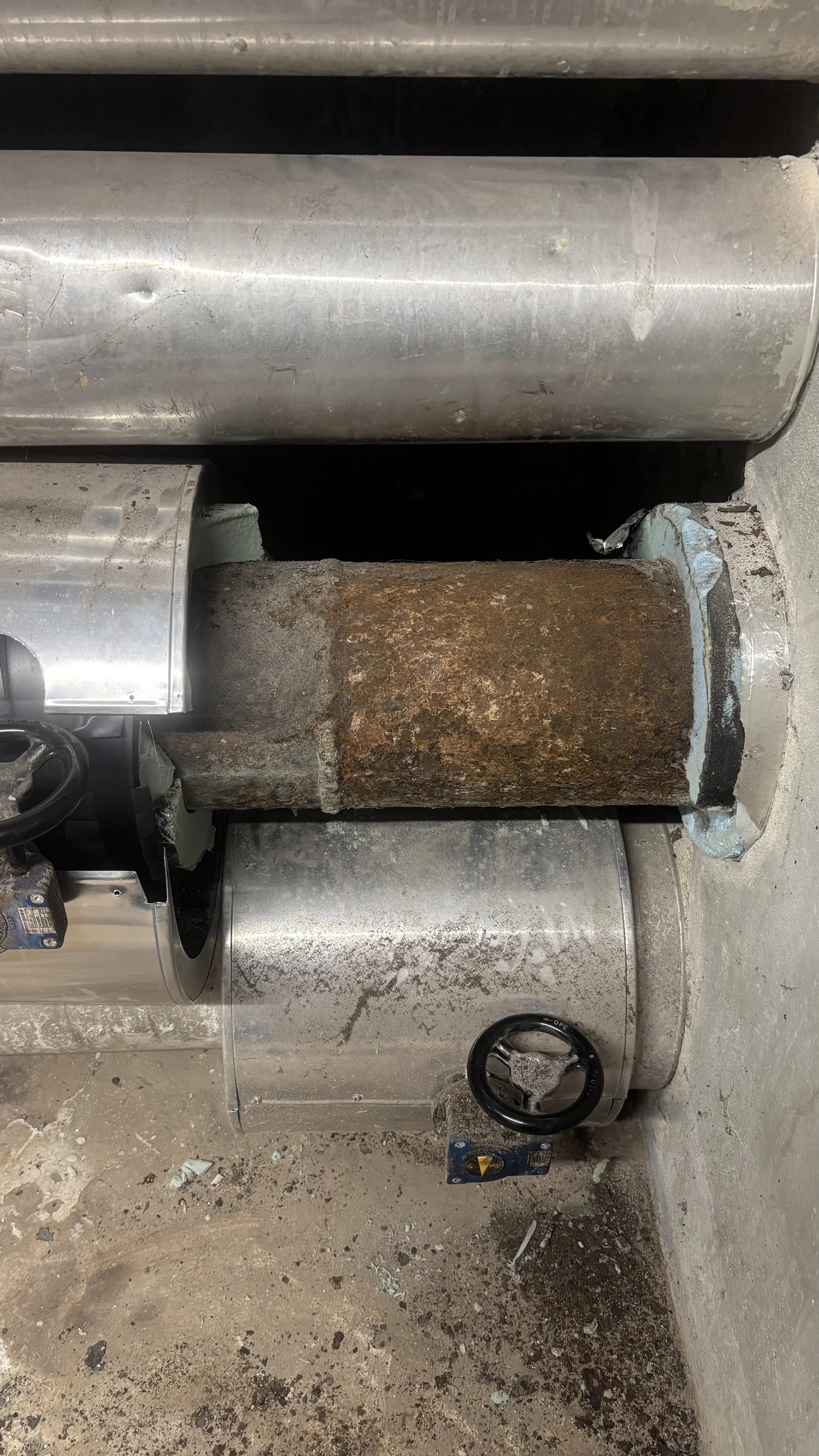 Une machine de traitement thermique avec un tube rouillé, entourée de récipients métalliques et de plomberie, dans un environnement industriel.