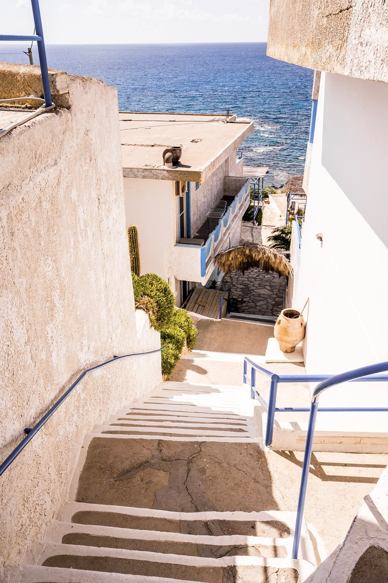 Weiße Treppen führen nach unten mit Blick auf das Meer in einer mediterranen Stadt mit weißen Gebäuden und blauen Akzenten.