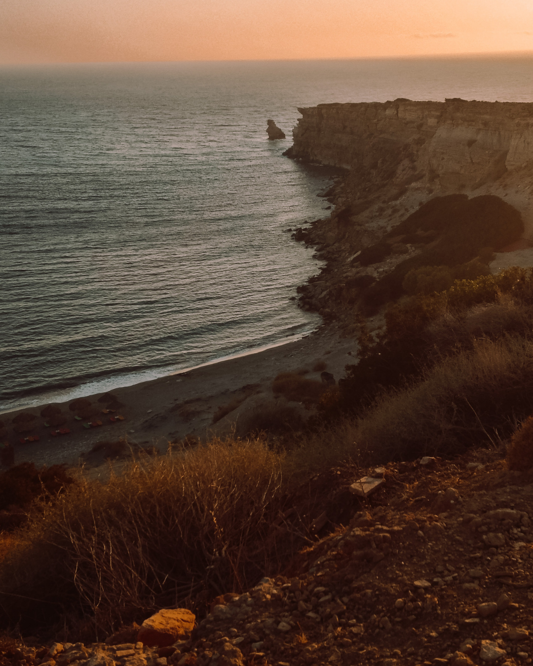 Aerial view of a coastal landscape with cliffs, a beach, and the ocean during sunset or sunrise.