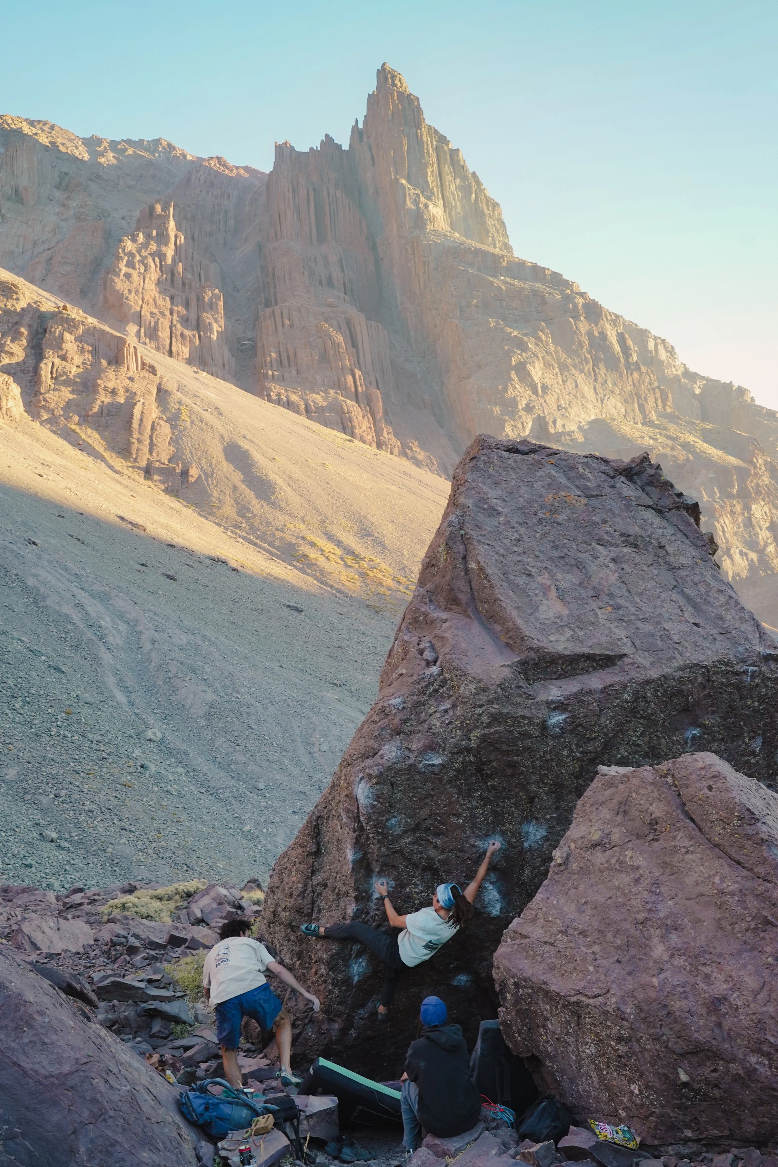 People bouldering and climbing on large rocks in a mountainous desert landscape during daytime.