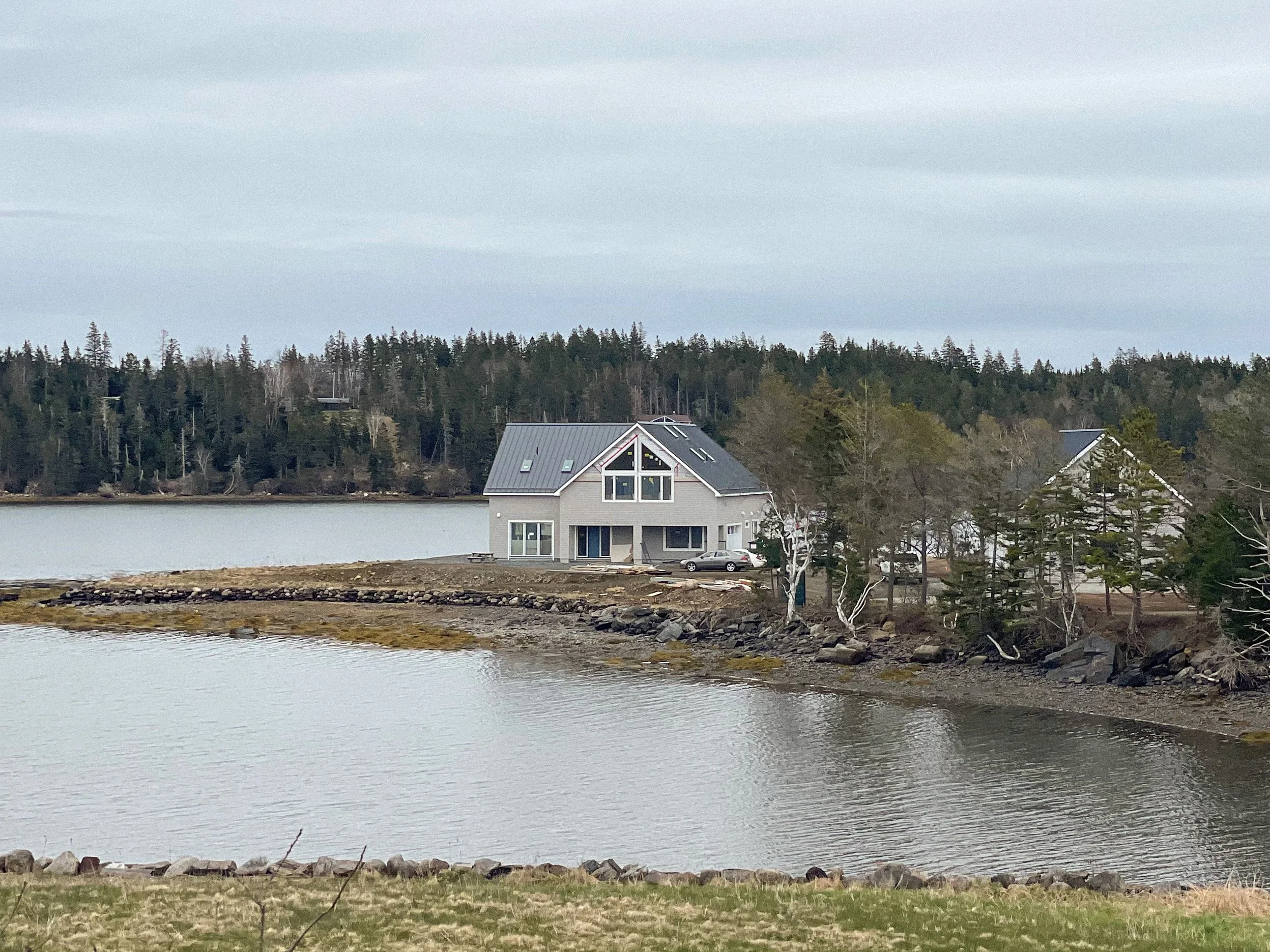 A house by the water with a wooded shoreline in the background, overcast sky.