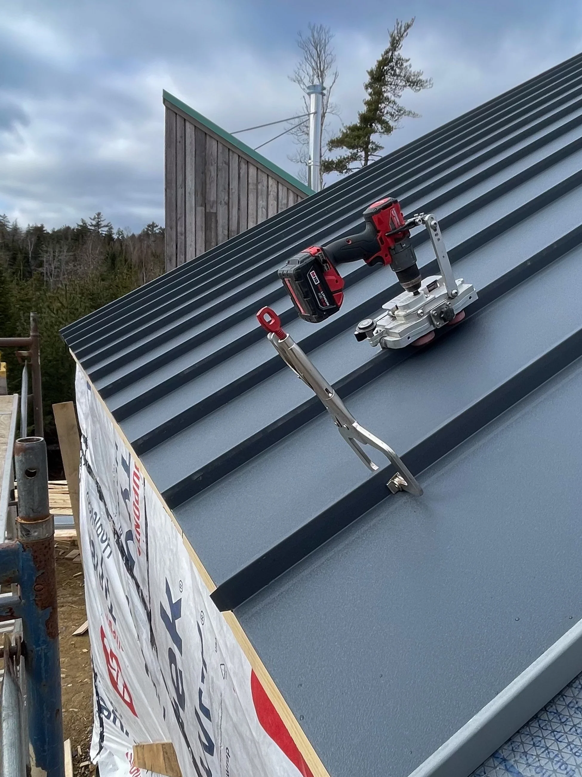 A metal roof under construction with a cordless drill and a hand tool attached to the roof.