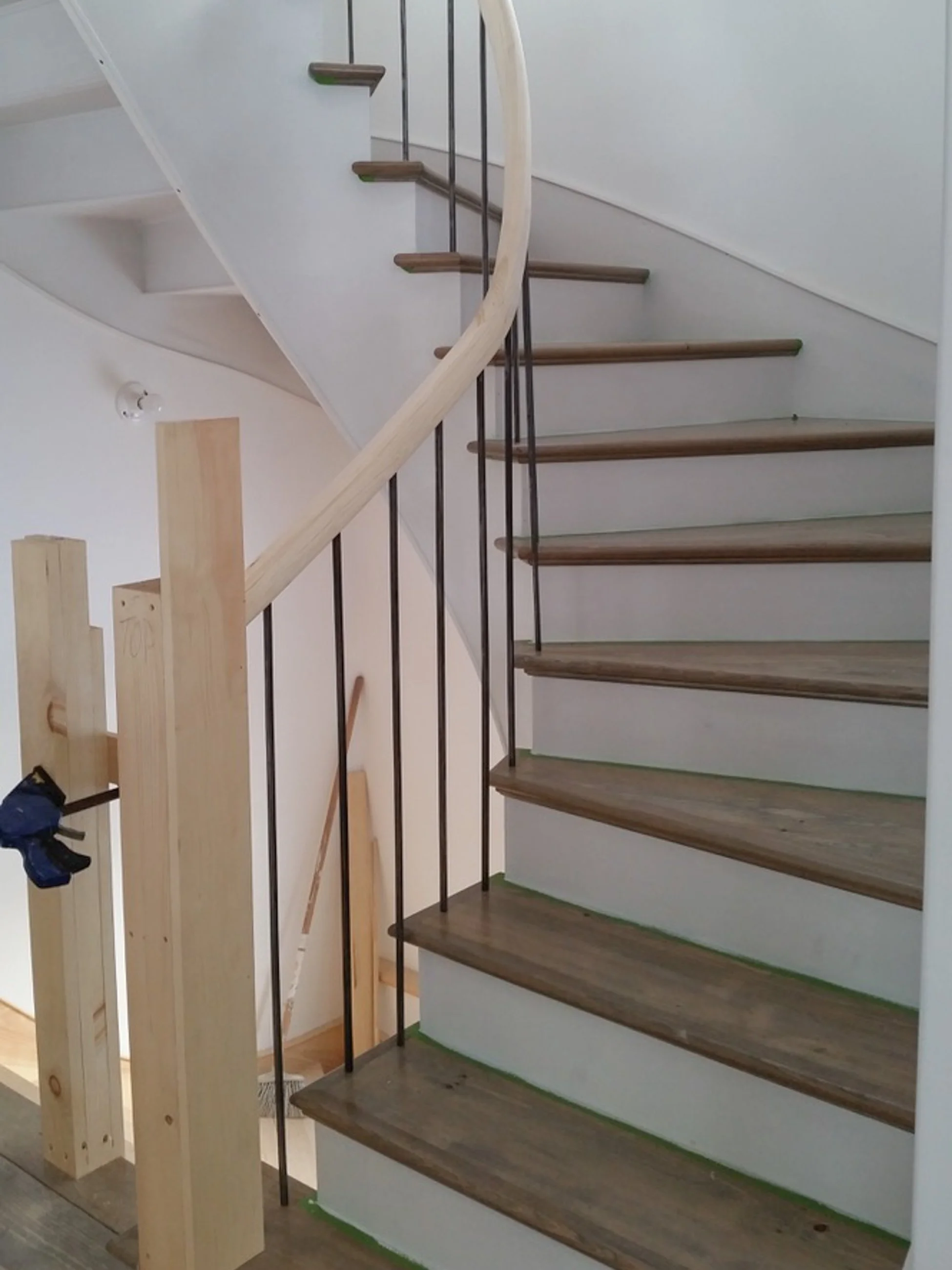 Interior staircase with wooden steps, a curved wooden handrail, and metal balusters, under construction in a house.