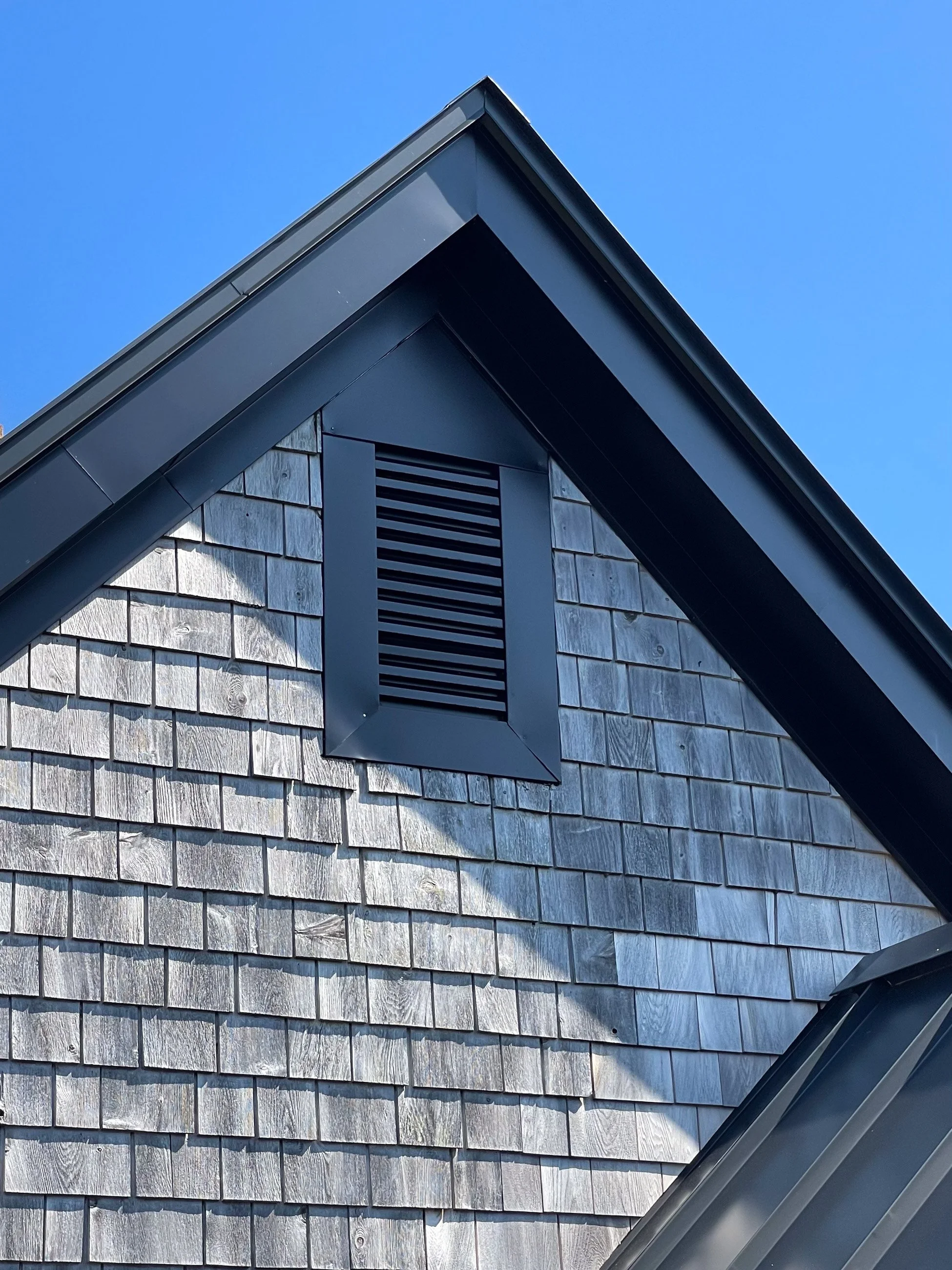 Close-up of a house's exterior showing a gable roof, shingled siding, and a vent on the upper part of the wall.