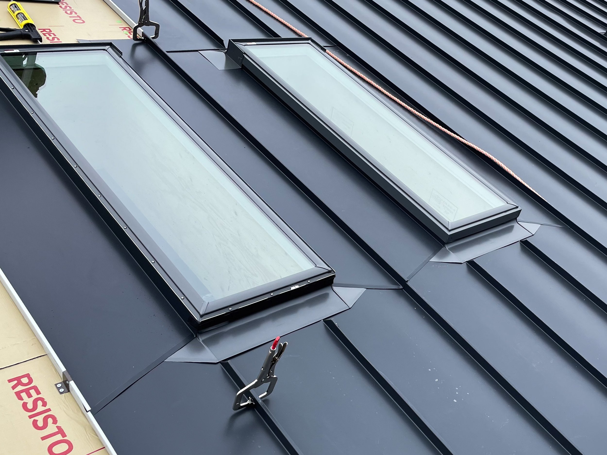 Metal roof with two skylights, a solar panel, and roofing tools.