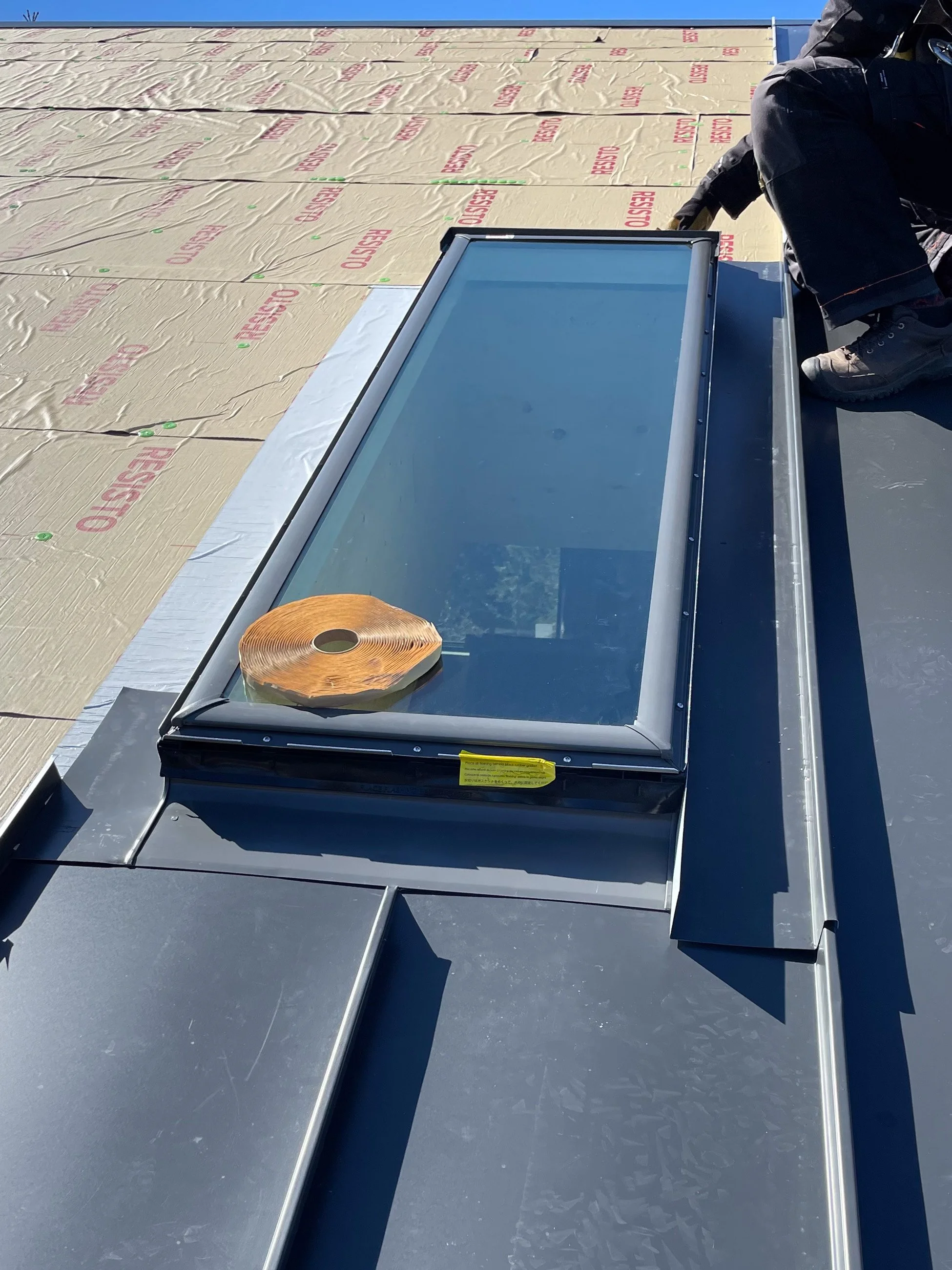 A person installing a skylight window on a building roof with insulation material labeled "FIBERGLASS" visible in the background.