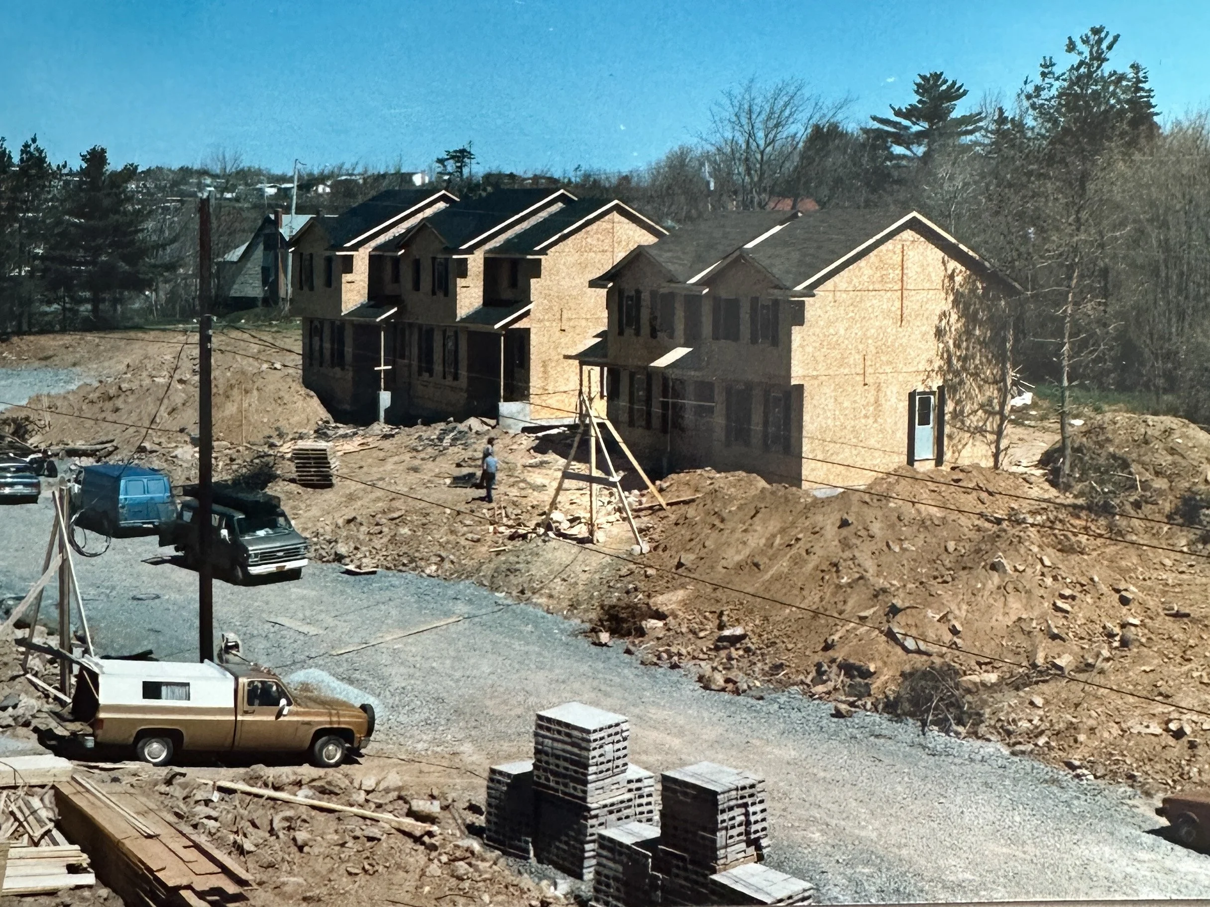 Construction site with several new houses under construction, dirt piles, construction vehicles, and building materials.