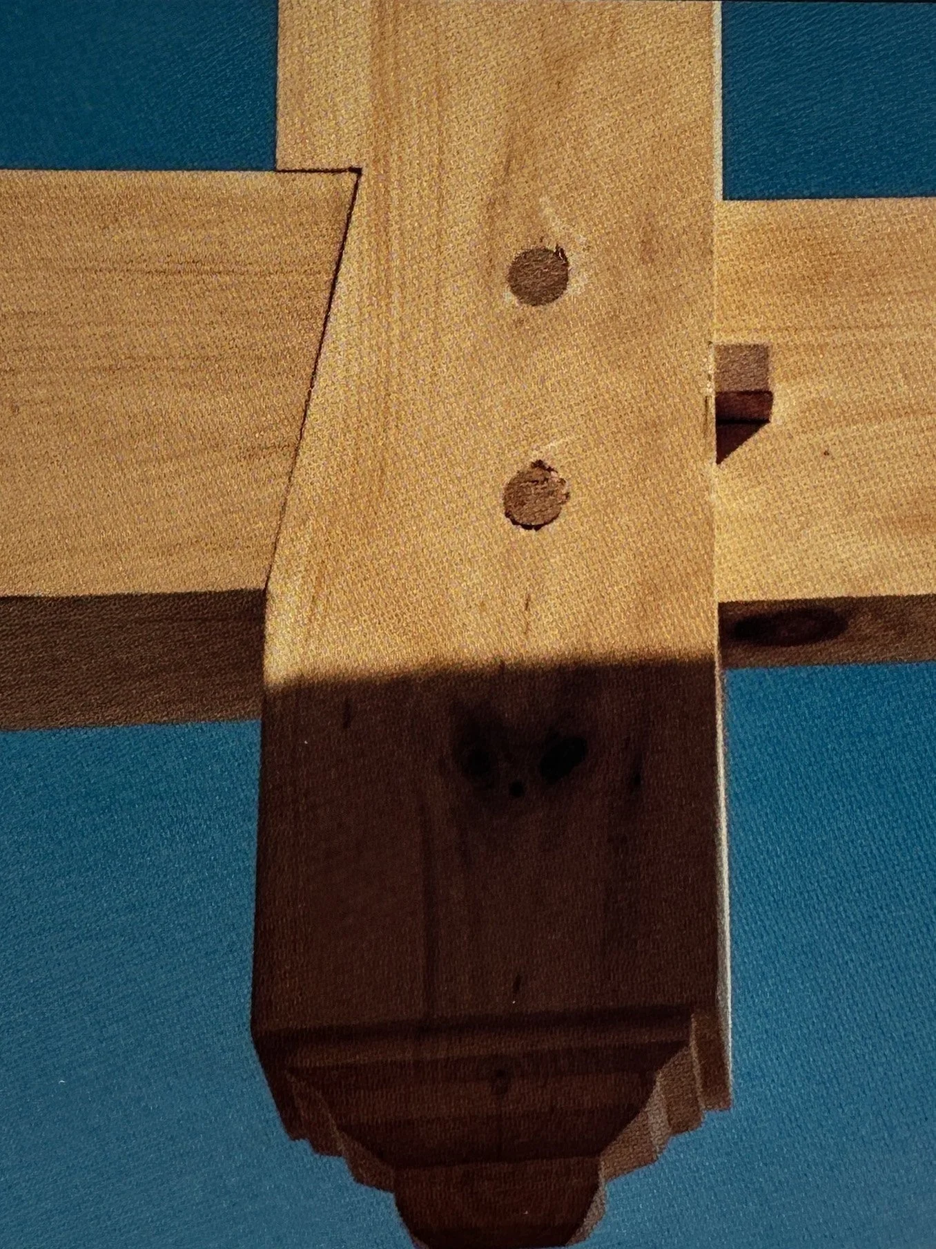 Close-up image of a wooden furniture piece with holes and a curved bottom edge, against a blue surface.