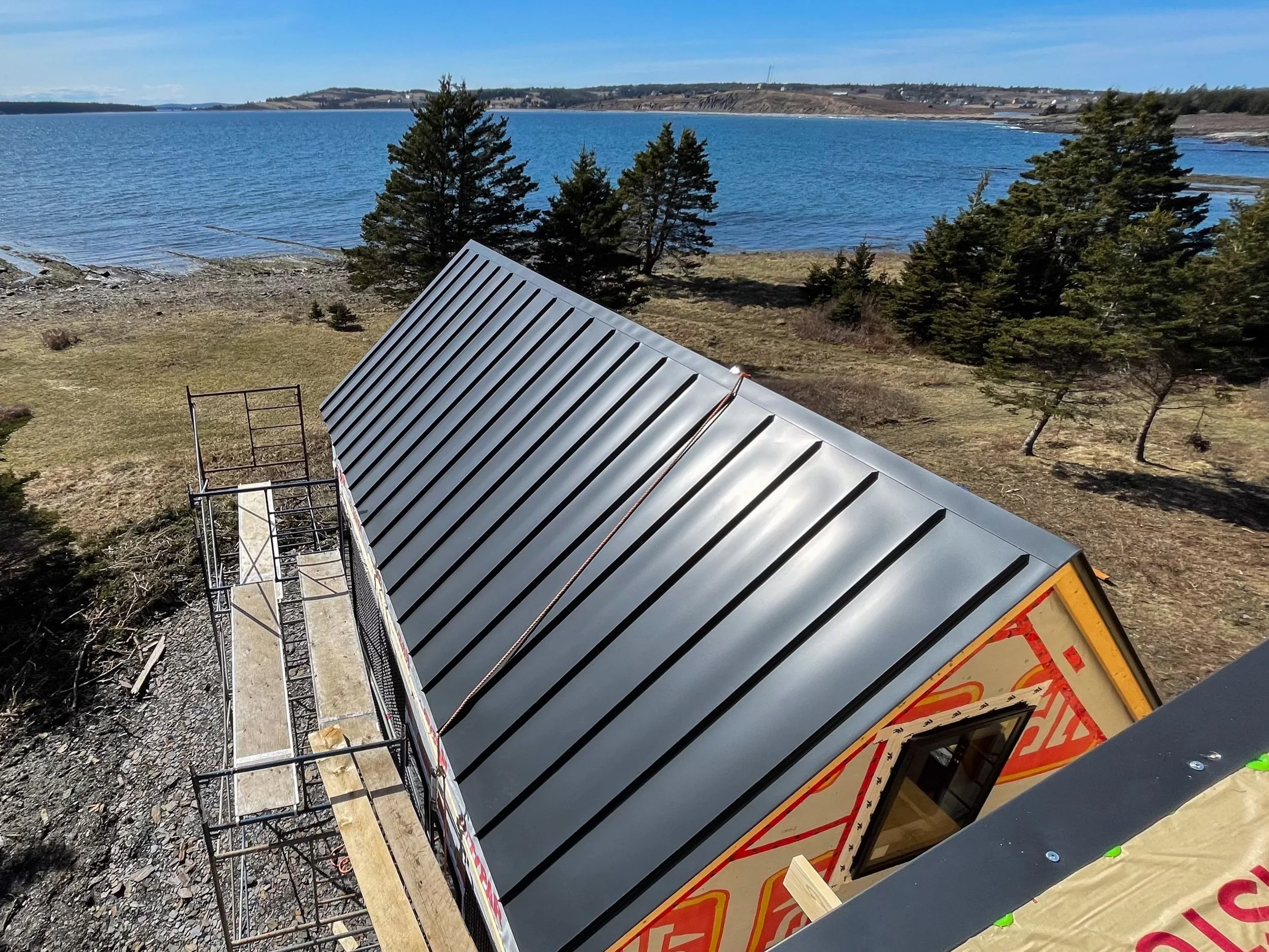 Construction site on a hill next to a lake with trees and rocky shoreline.