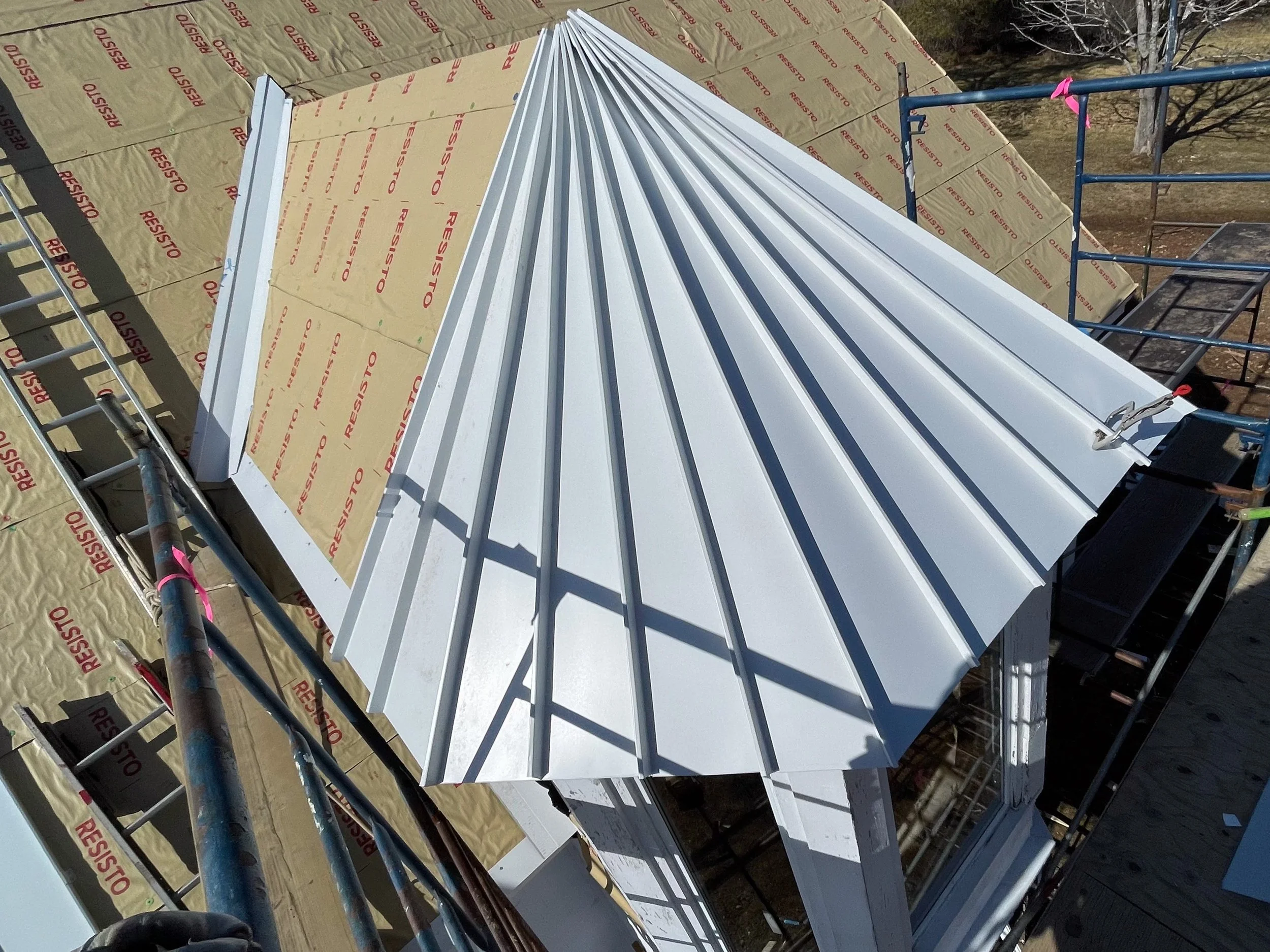 Roof under construction with metal panels and scaffolding, insulation material labeled 'Resisto' visible on the roof surface.