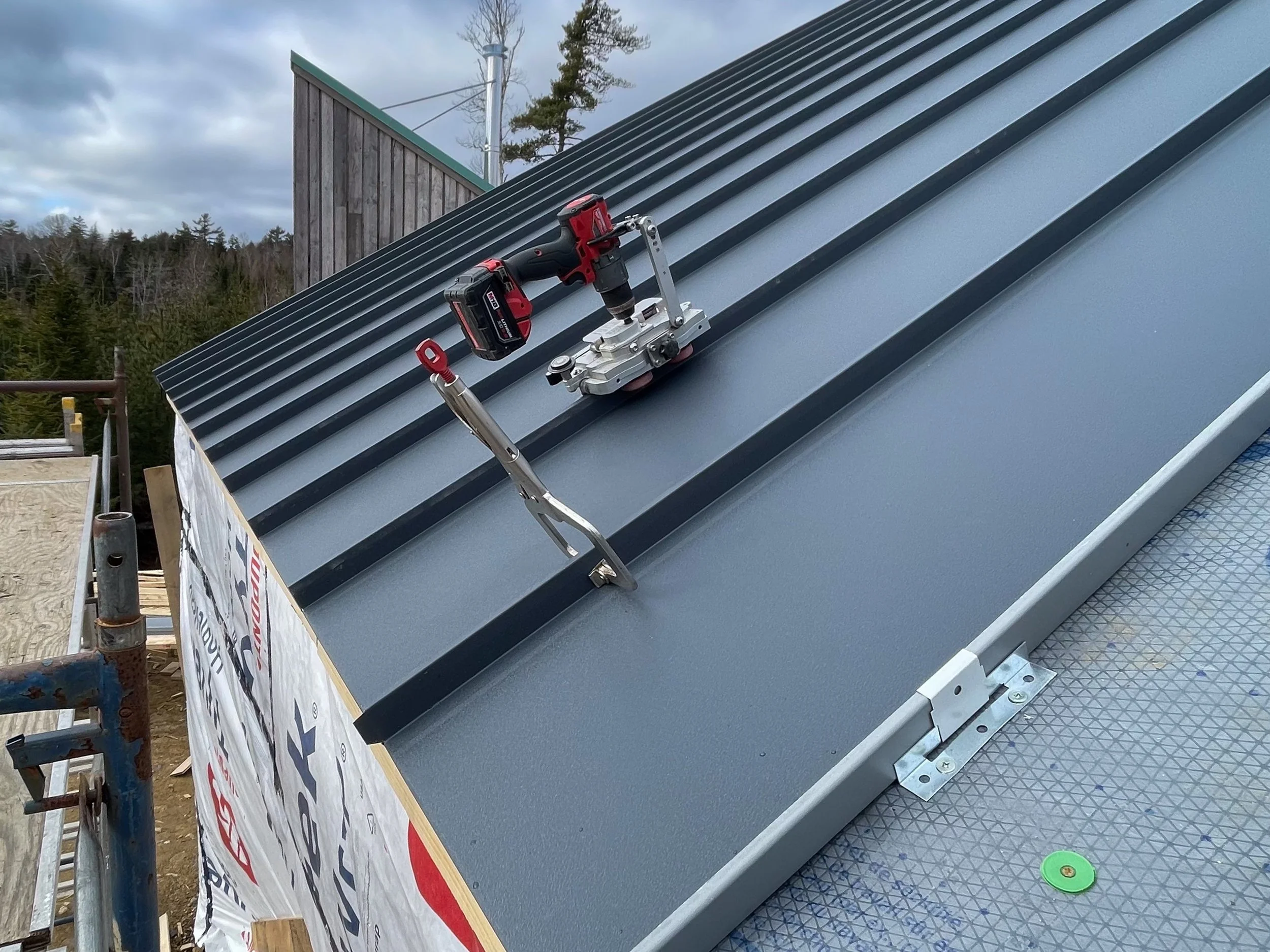 View of a metal roof with a cordless drill, a metal tool, and a mounting bracket on top, possibly during installation.