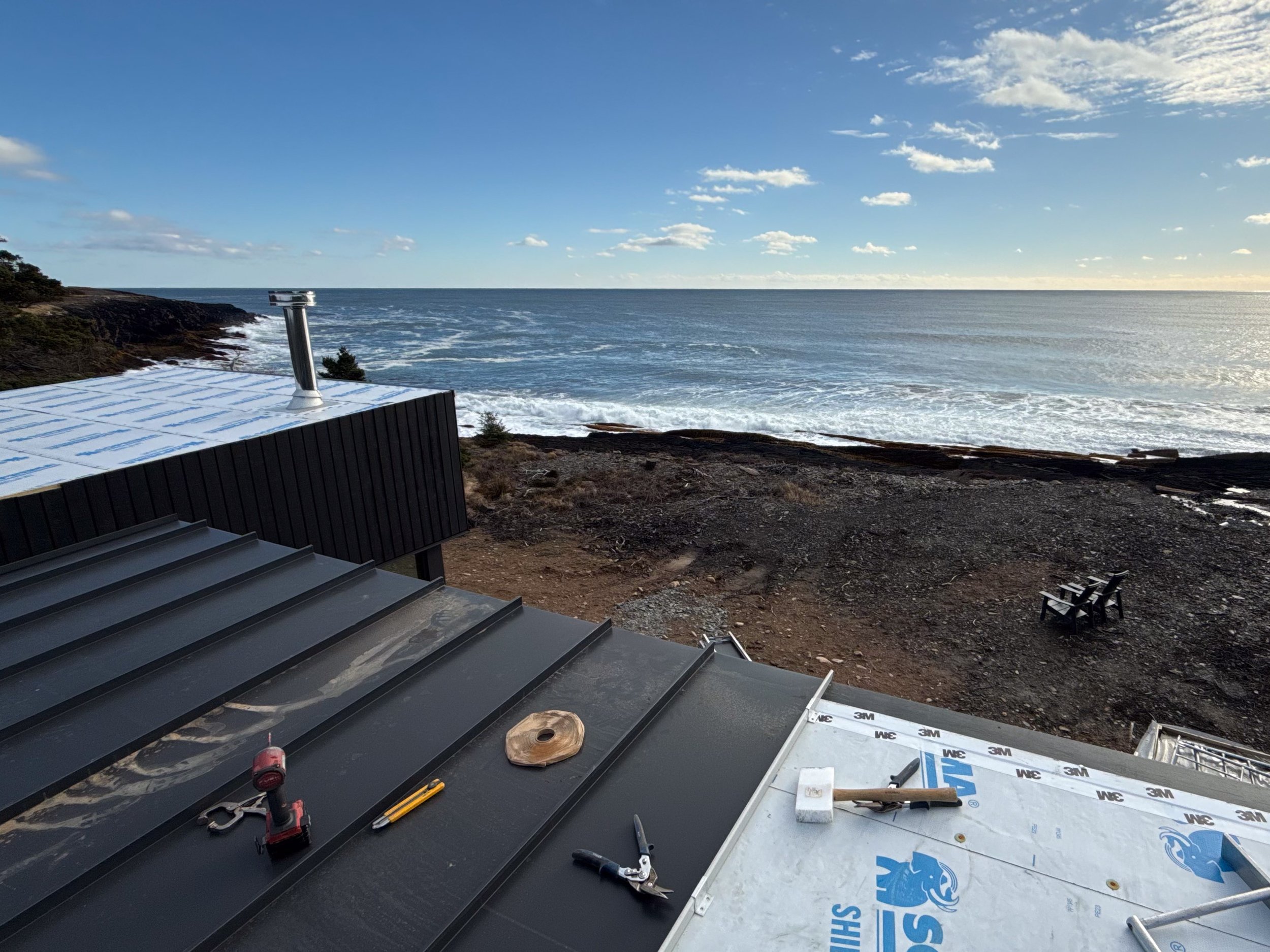 Construction on a building overlooking the ocean with tools and materials on the roof.