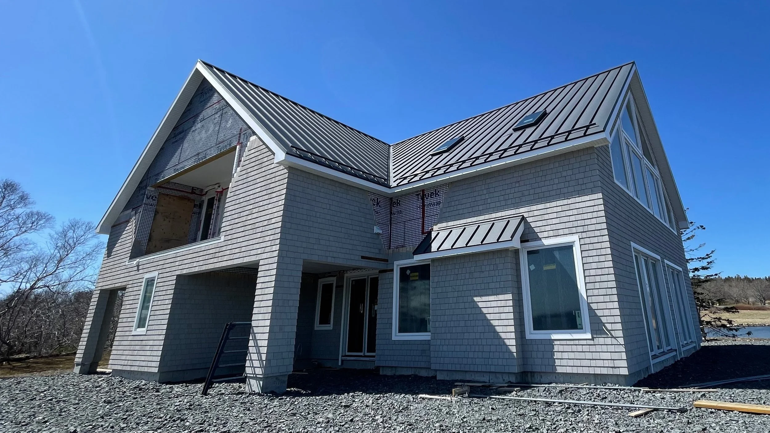 Newly constructed multi-story house with gray siding and metal roof, under a clear blue sky.