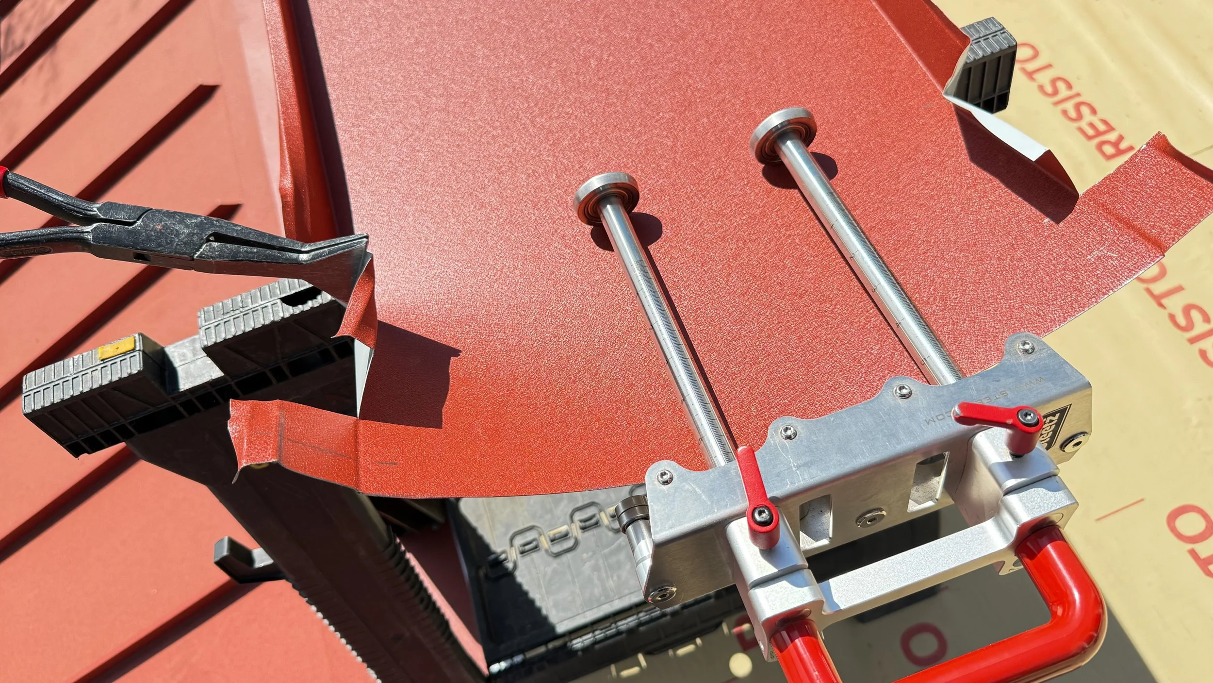 A workbench with a red, textured circular metal sheet, metal rods, and clamps, with tools and measuring devices attached.