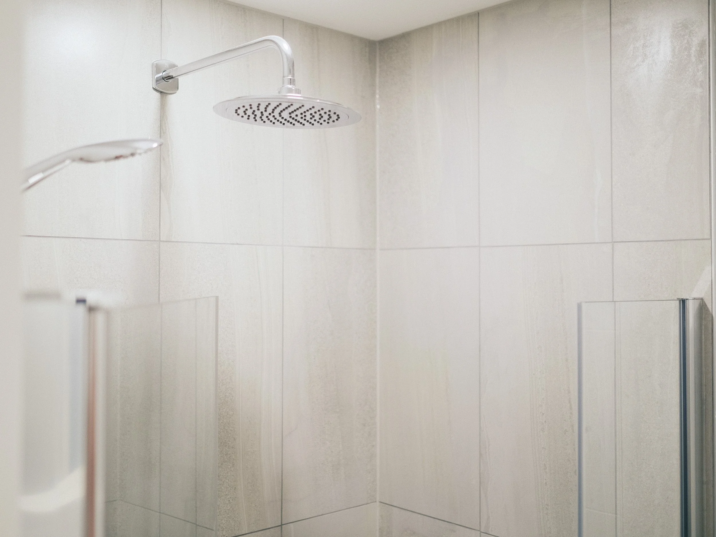 A walk-in shower with two overhead shower heads on a tiled wall.