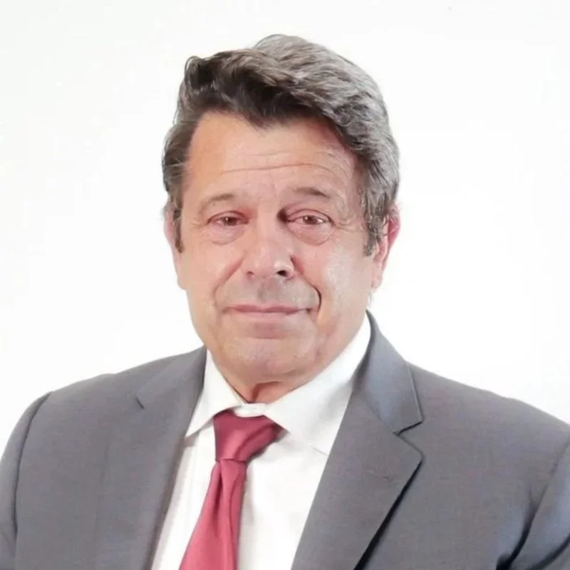 A middle-aged man wearing a gray suit, white shirt, and red tie, with a neutral expression, short hair, and a slightly confident pose.