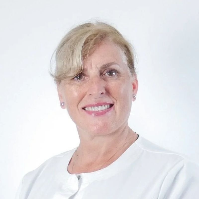 Portrait of a middle-aged woman with short blonde hair, wearing a white top, smiling, against a plain white background.
