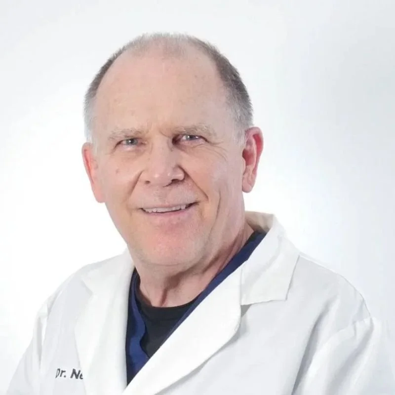 A middle-aged man with short hair wearing a white medical coat, smiling against a white background.