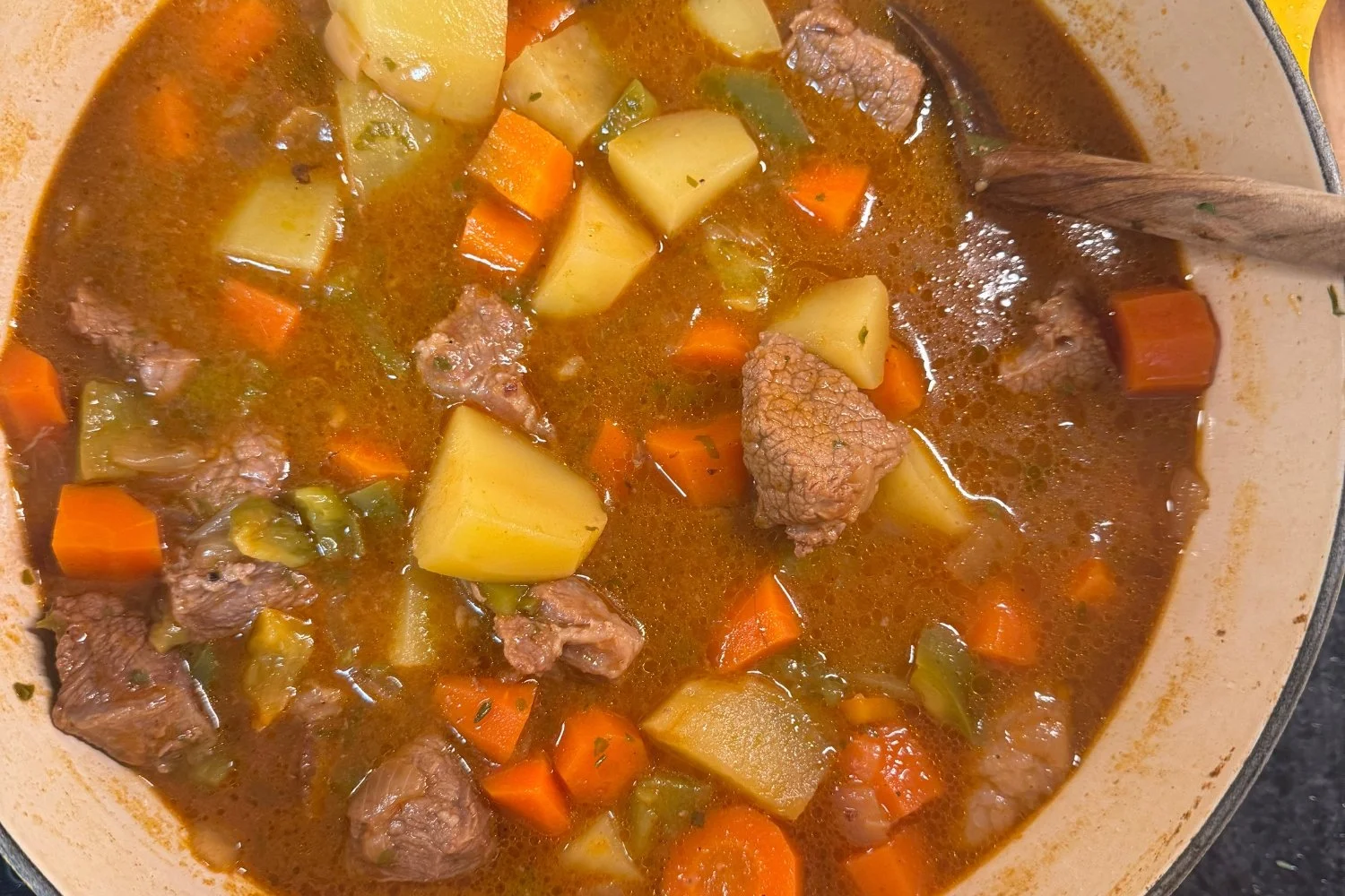 Beef stew with potatoes and carrots cooking in a yellow Dutch oven on a cook day.