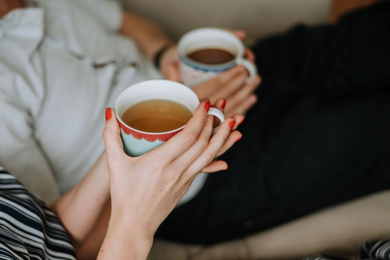 A new mother and her support person sharing a cup of warm tea or broth while she rests postpartum.