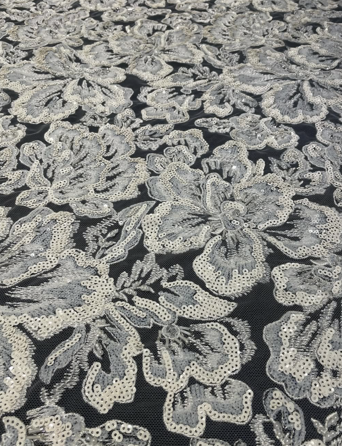Tissu noir avec des motifs floraux en sequins argentés.