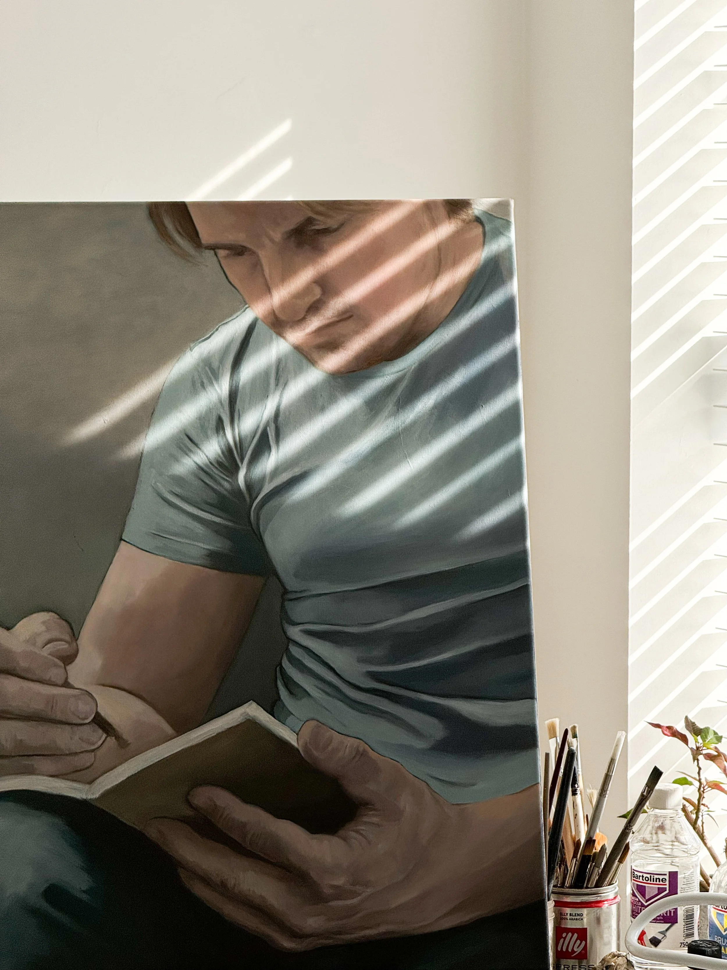 Close-up of a painting of a man in a gray t-shirt holding a notebook and writing with a pen, with sunlight streaming through blinds casting shadows on his face and body.